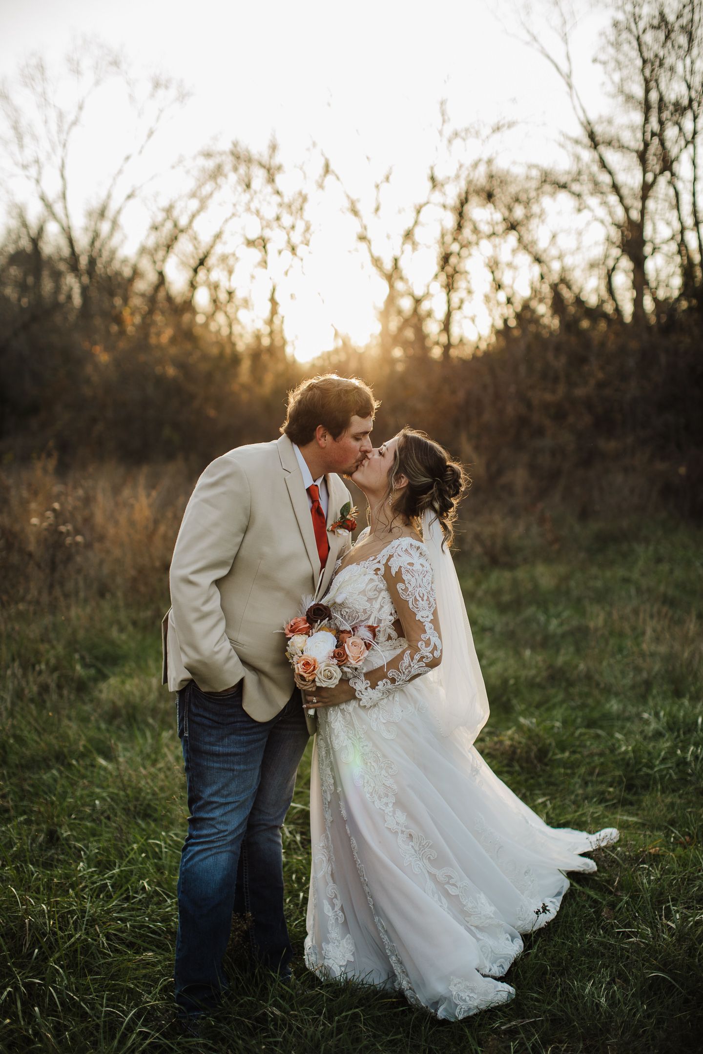 A romantic sunset wedding photoshoot in a grassy field with golden light filtering through autumn trees.