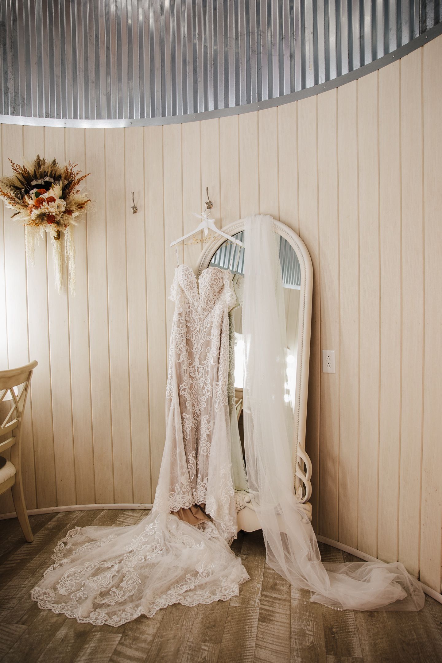 A delicate lace wedding dress hangs elegantly against a white paneled wall with mirrors.