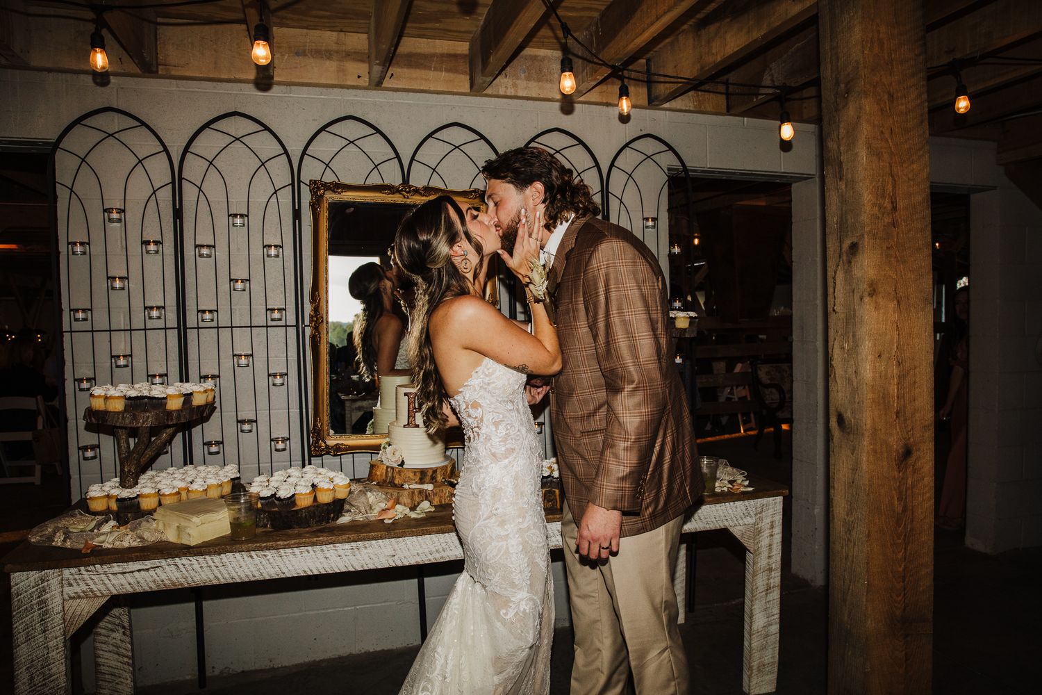 Wedding reception in rustic venue with exposed wooden beams and decorative lighting.
