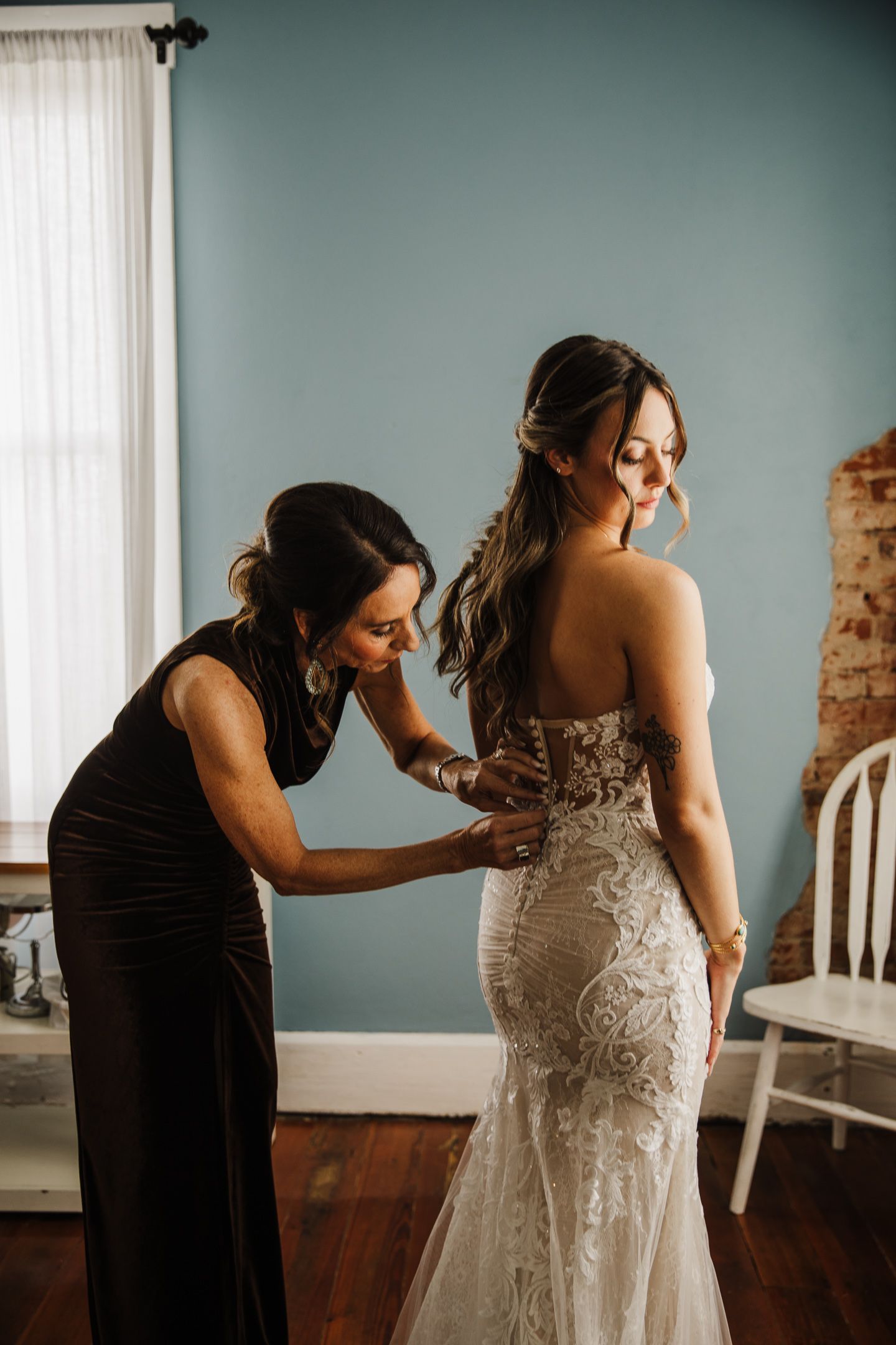 A wedding dress being buttoned up in an elegant room with teal walls.