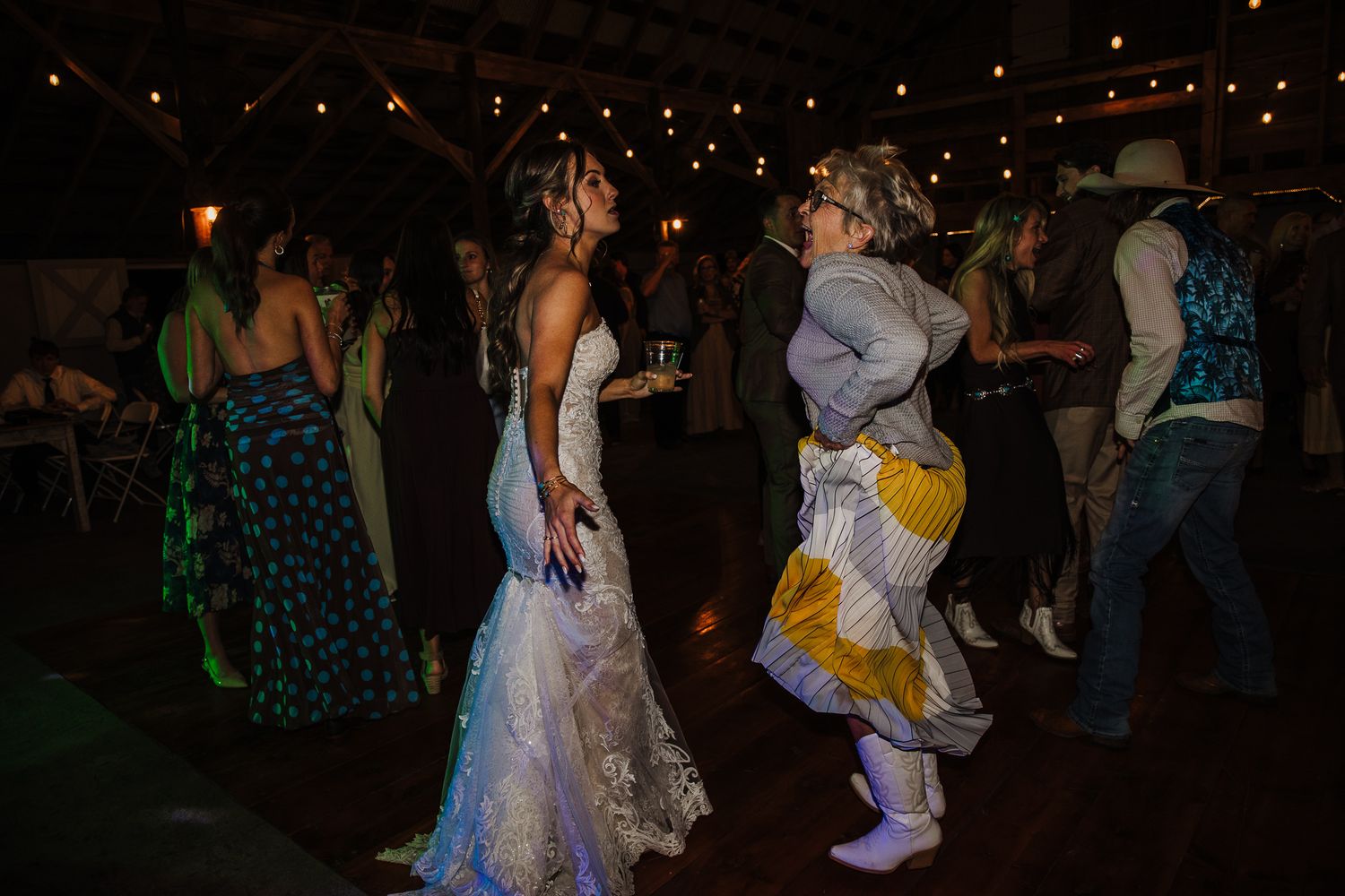 Wedding guests dance and celebrate on dimly lit reception dance floor.
