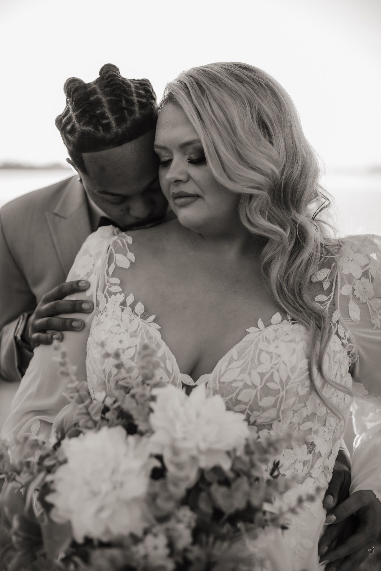 Intimate black and white portrait of newlyweds embracing with bouquet.