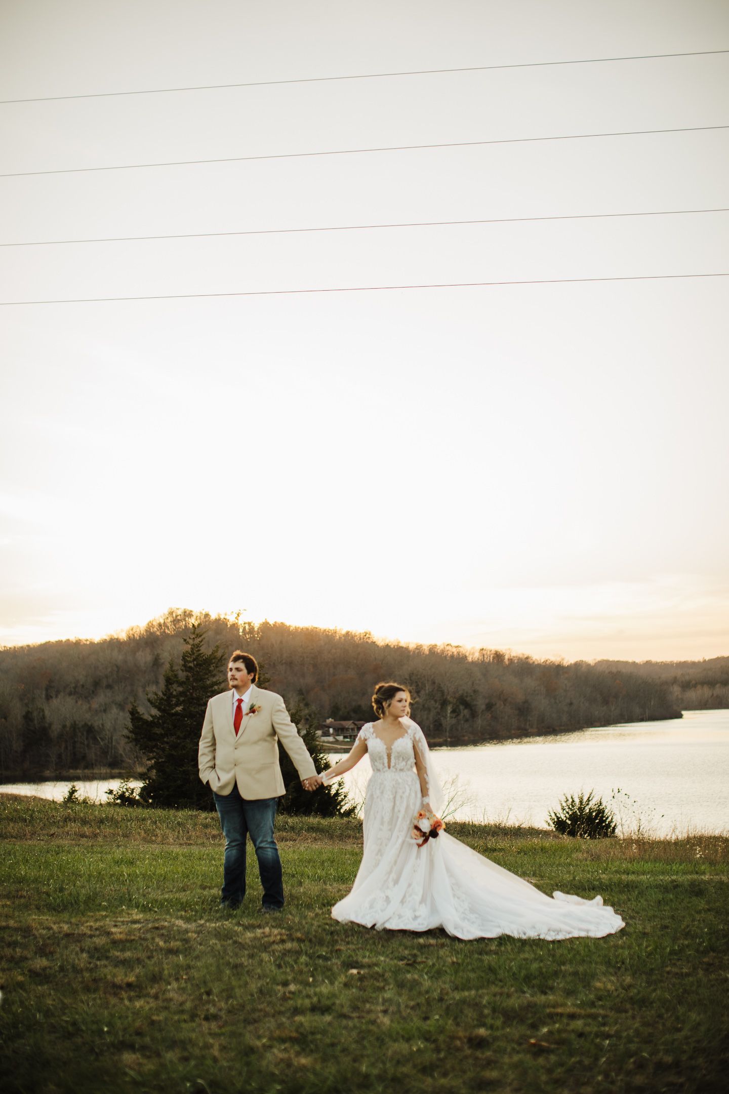 A romantic sunset photoshoot on a grassy hill overlooking a serene lake with autumn trees in the background.