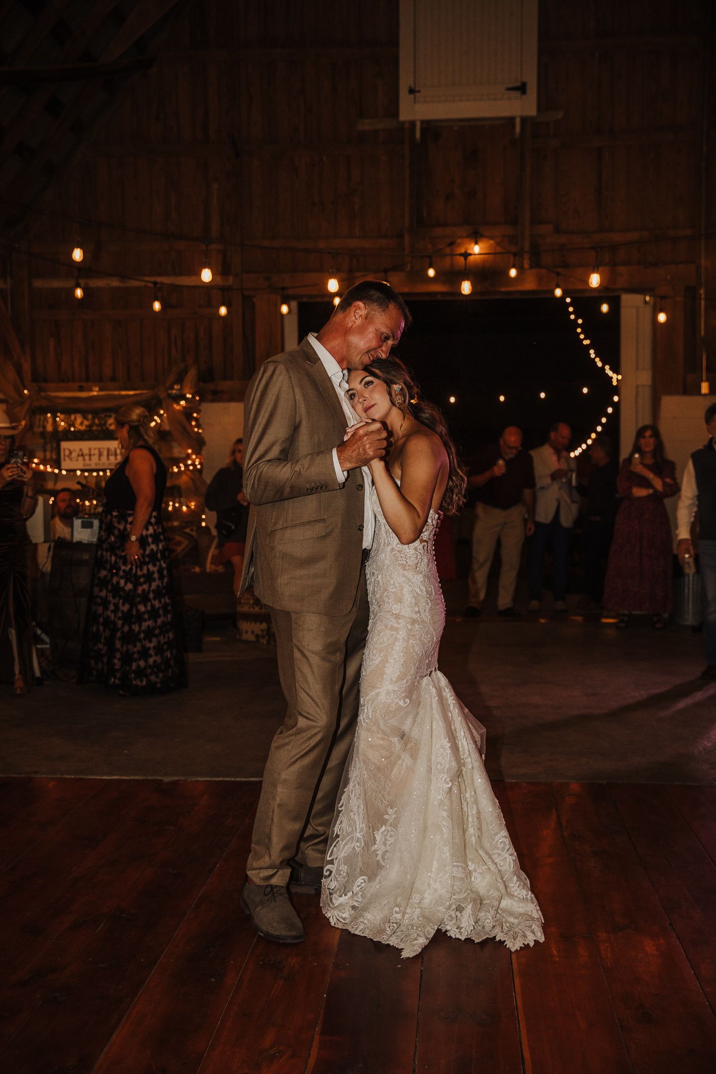 First dance moment in a rustic barn venue with warm string lights creating ambient lighting.