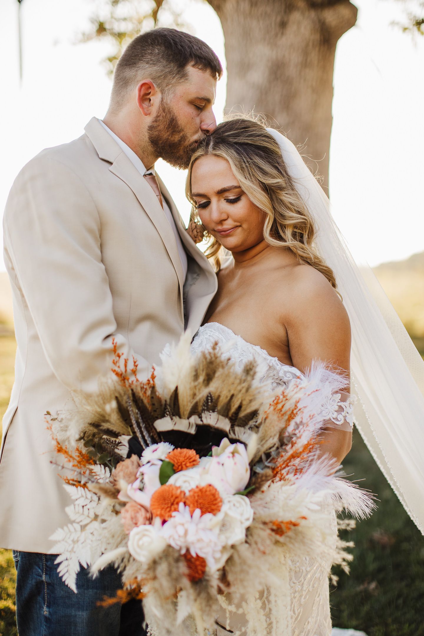 Romantic wedding couple with boho-inspired dried flower bouquet in warm sunset light.
