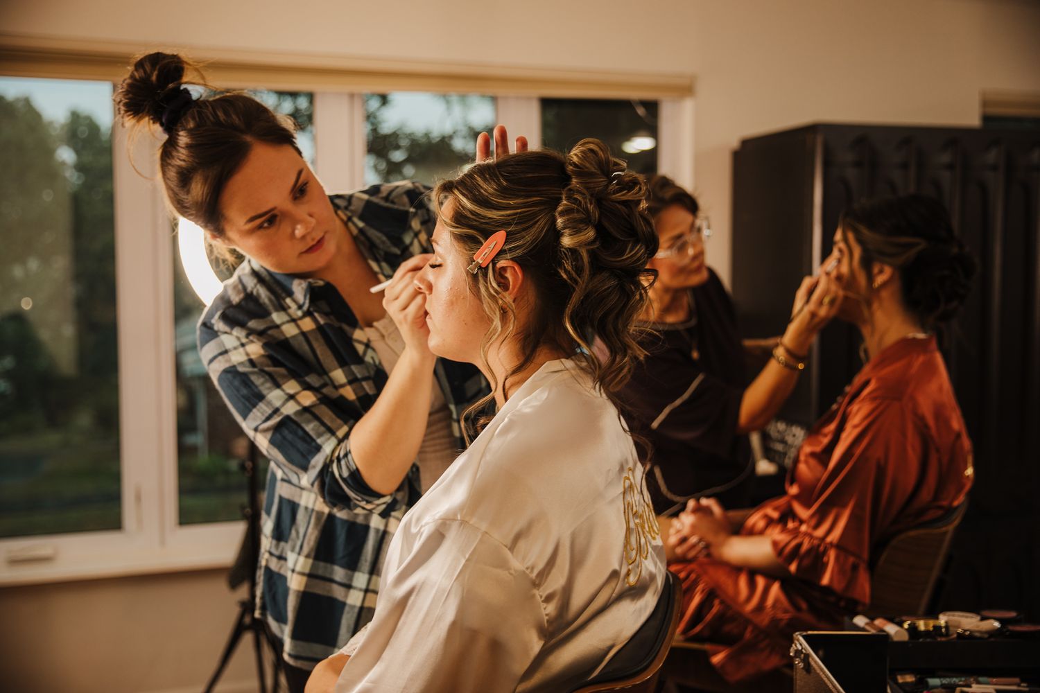 Wedding preparation scene with stylists working in a sunlit room.