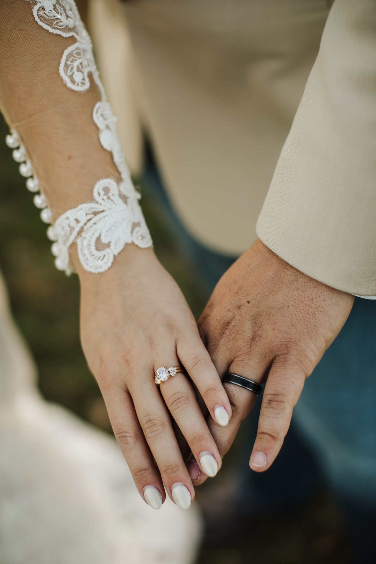Close-up of newlywed hands showing wedding rings and lace sleeve detail.