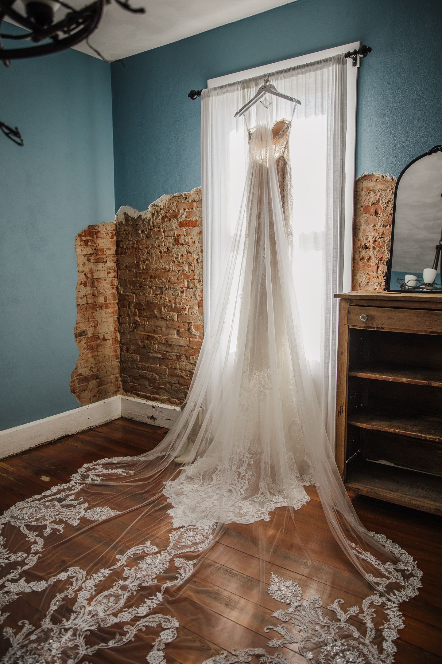 Elegant lace wedding dress with long train displayed hanging in a room with blue walls.
