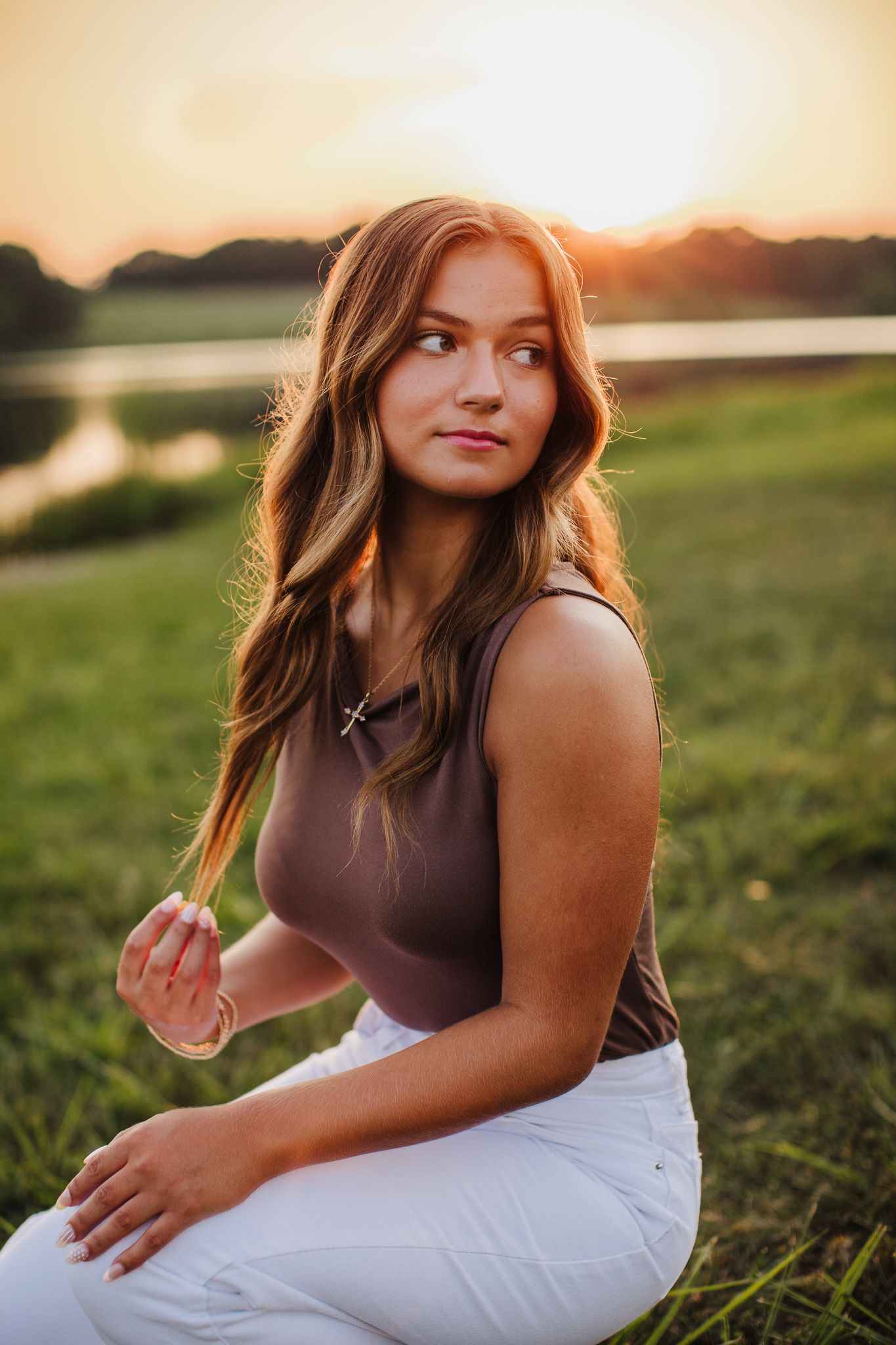 Young woman in casual attire poses in golden sunlit field during sunset photoshoot.