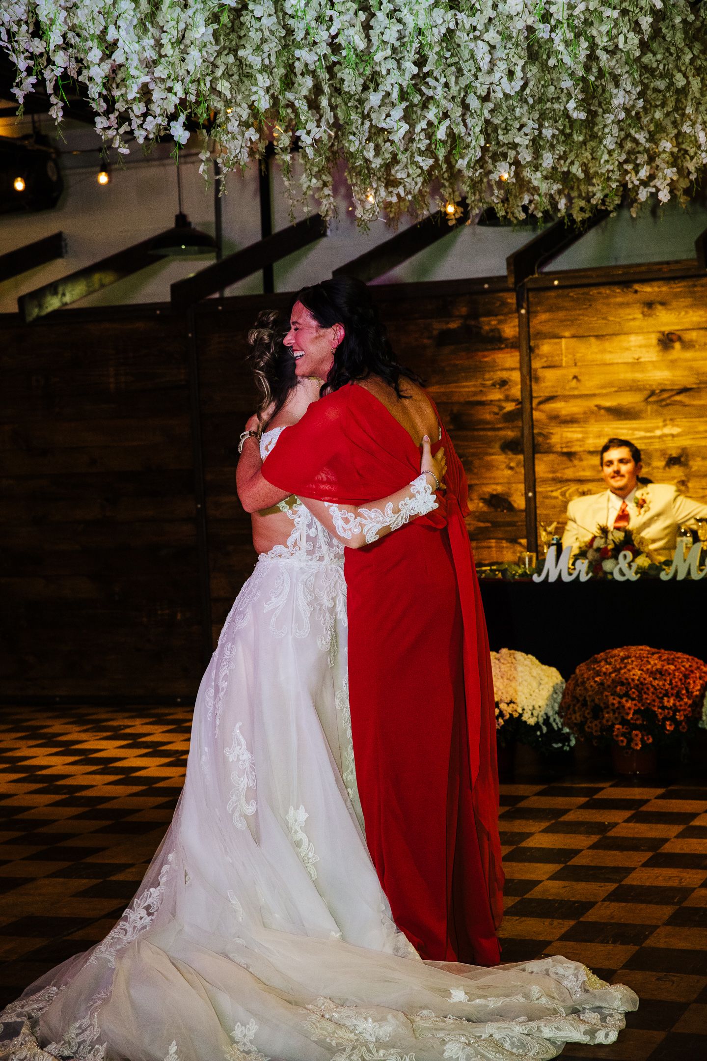Wedding dance moment under hanging white floral installations with checkered floor.