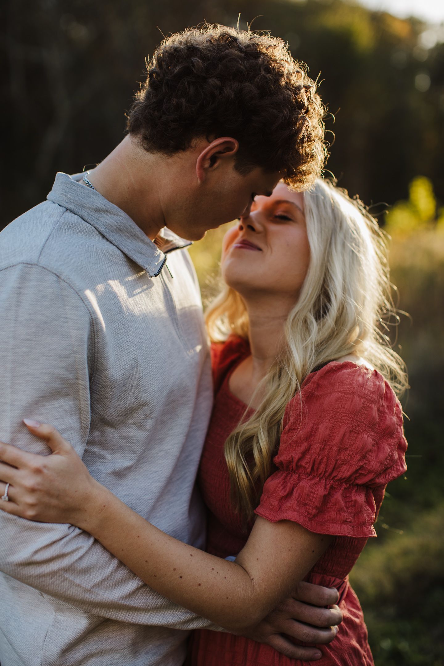A couple shares an intimate embrace in soft natural lighting during sunset.