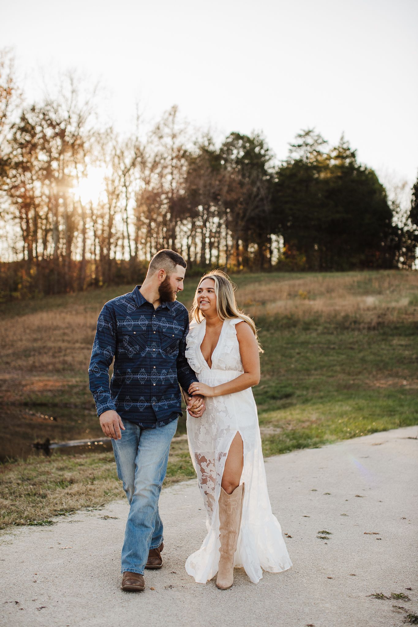 Couple walking together on a dirt path during a countryside photoshoot at sunset.