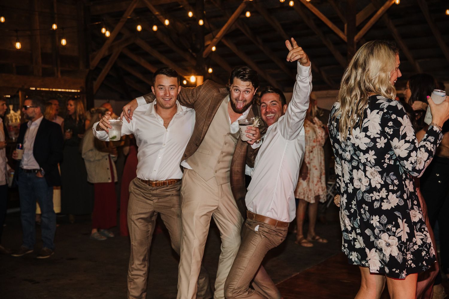 Wedding guests dance and celebrate in a dimly lit reception venue with string lights overhead.