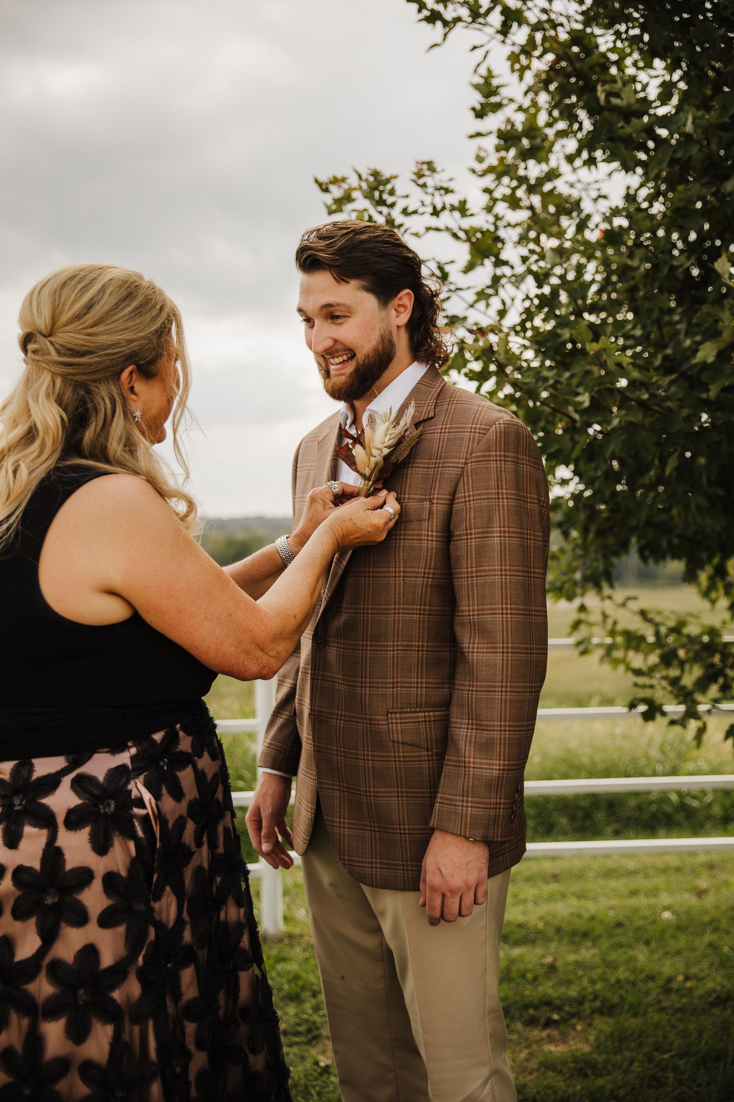A couple shares an intimate first look moment outdoors, with the person wearing a brown plaid suit jacket.