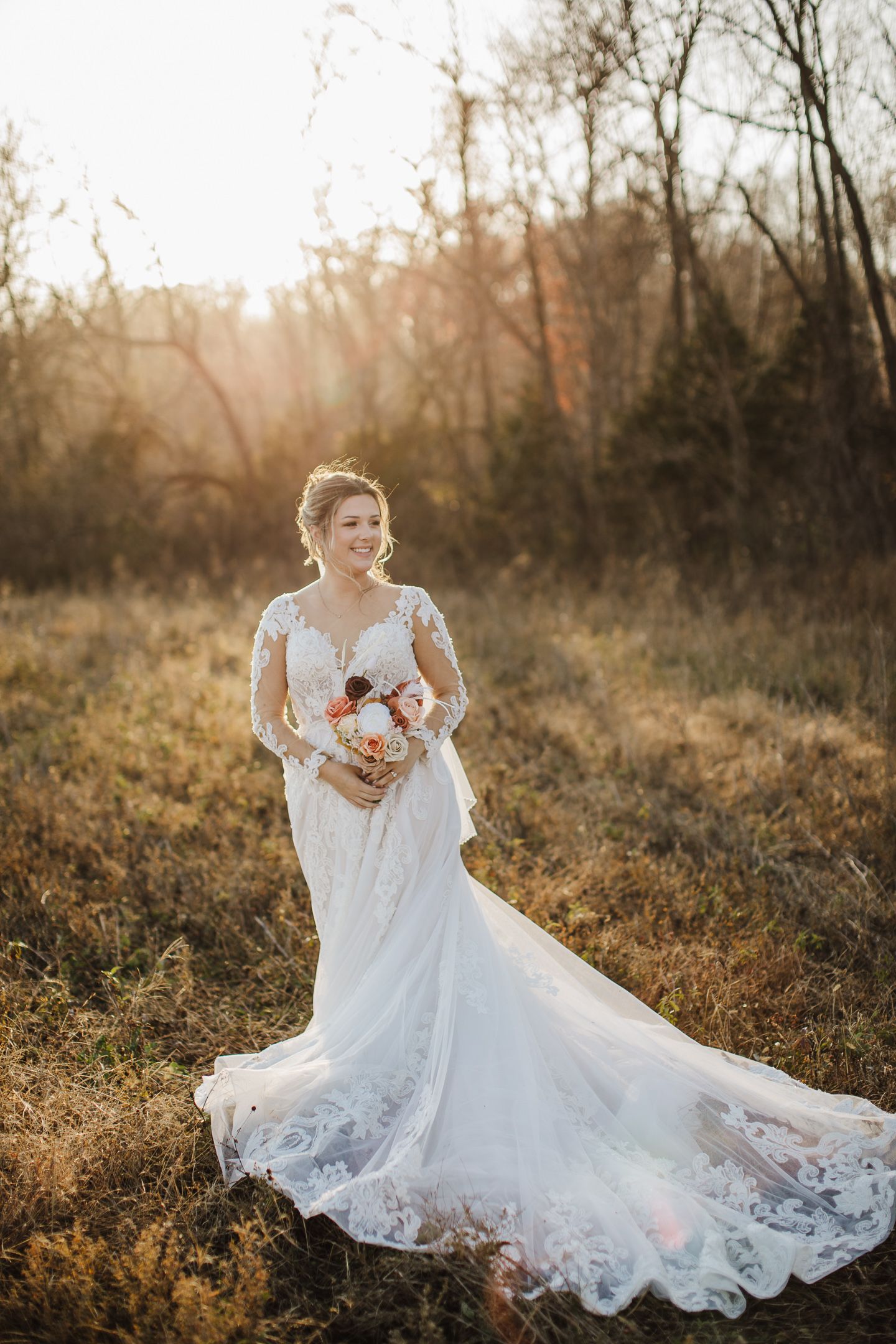 A bride in an elegant lace gown twirls gracefully in a sun-drenched autumn forest clearing.