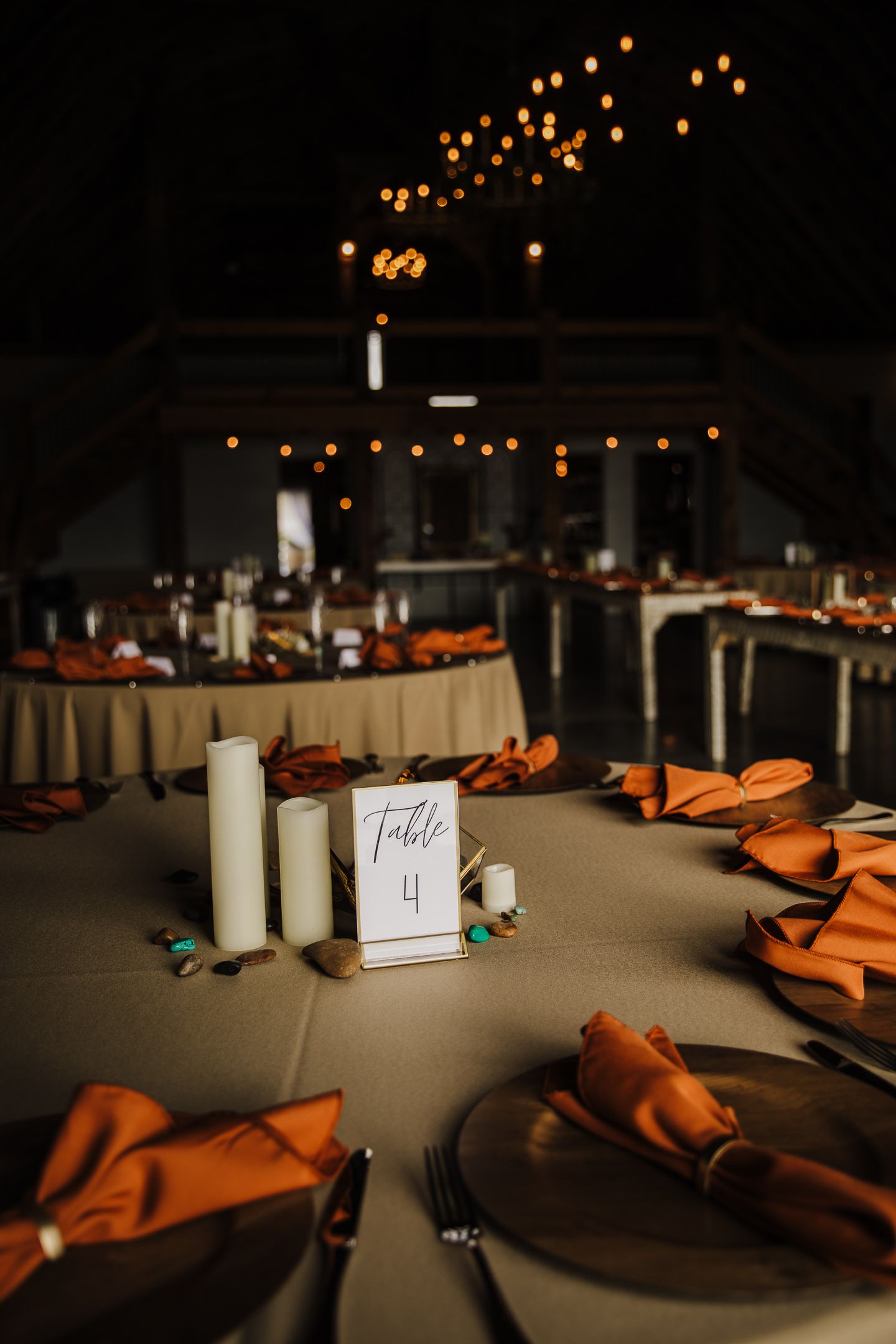 Table setting with orange napkins and string lights creating an intimate ambiance at an indoor event.