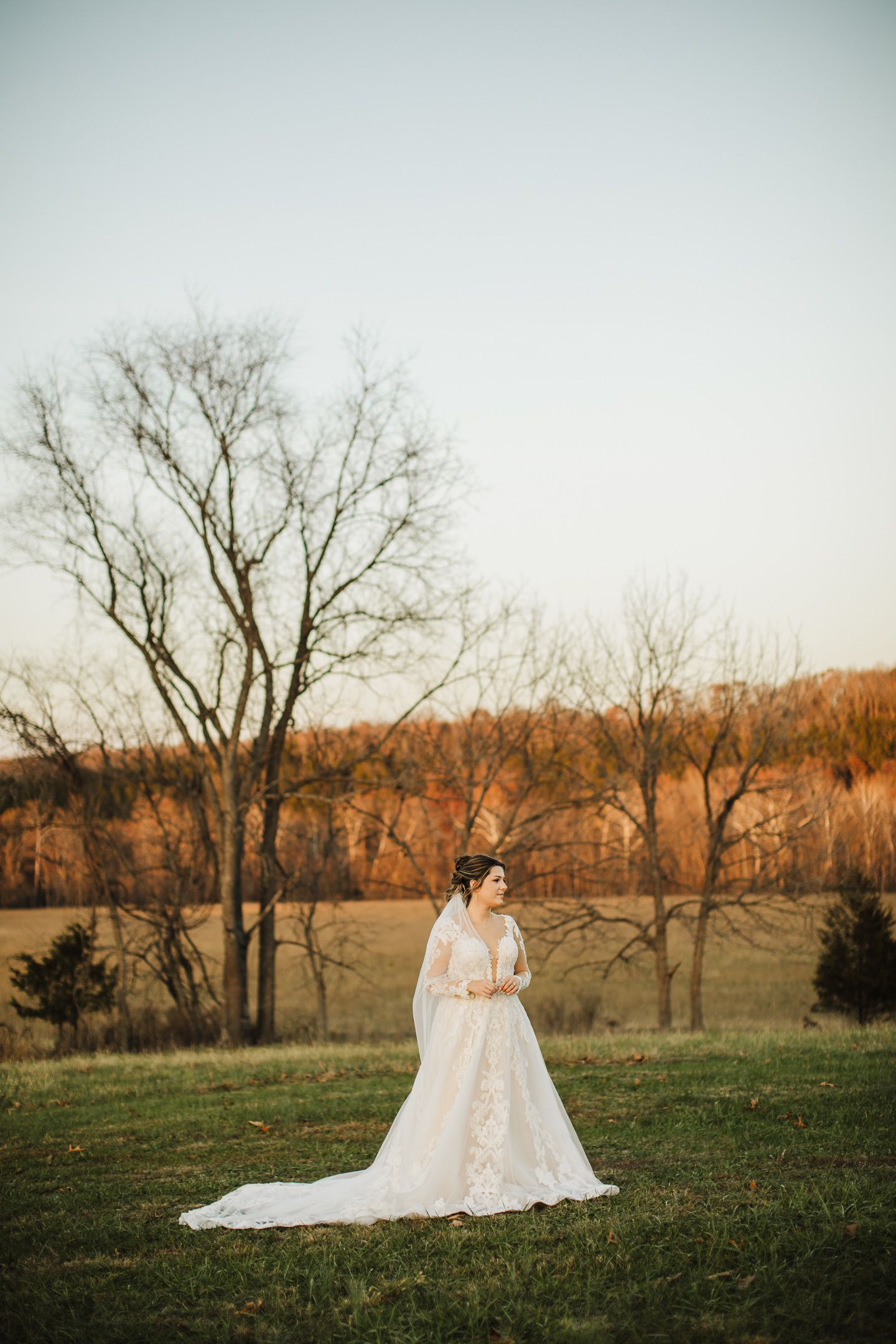 A scenic autumn wedding photo session in a field with bare trees and golden light creating a dreamy atmosphere.