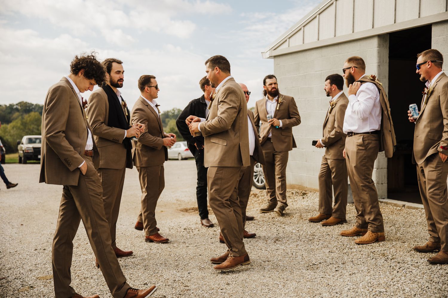 Groomsmen in brown suits line up on gravel path for wedding photo.
