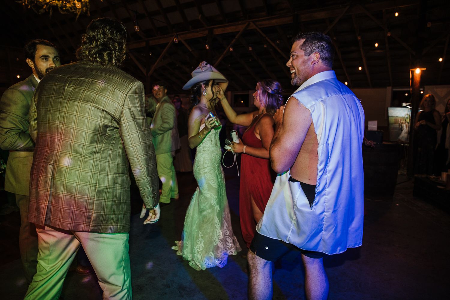 Wedding reception guests dancing under colorful lights in a dark venue.