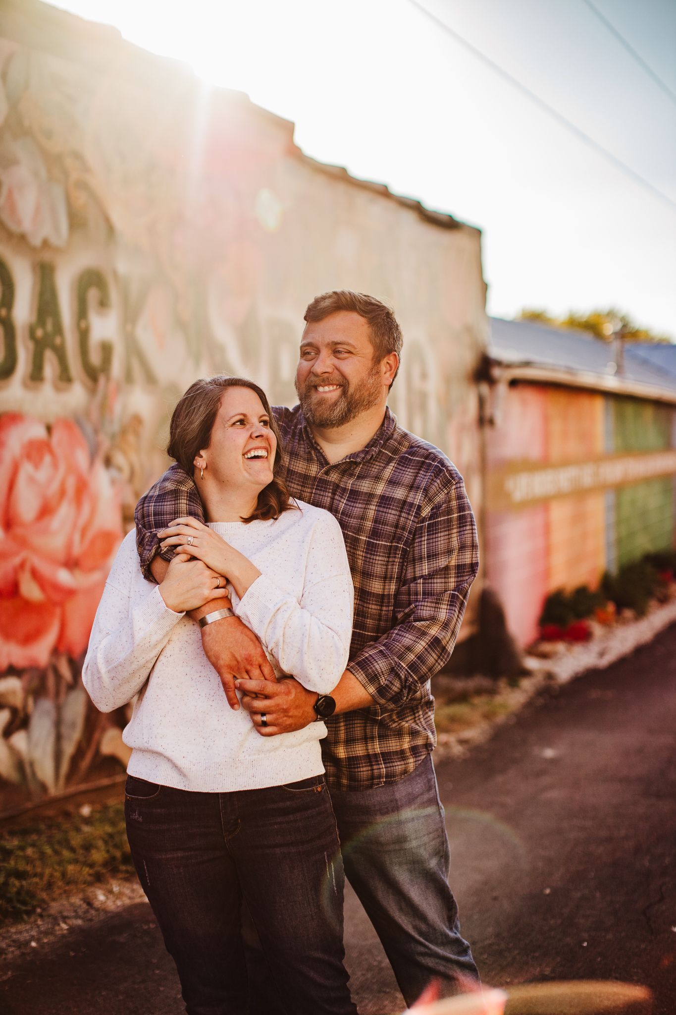 Couple sharing intimate laughs against graffiti wall during sunset photoshoot.