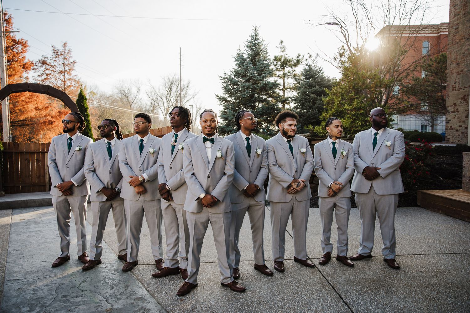 Groomsmen in light gray suits stand in a formal line outdoors.