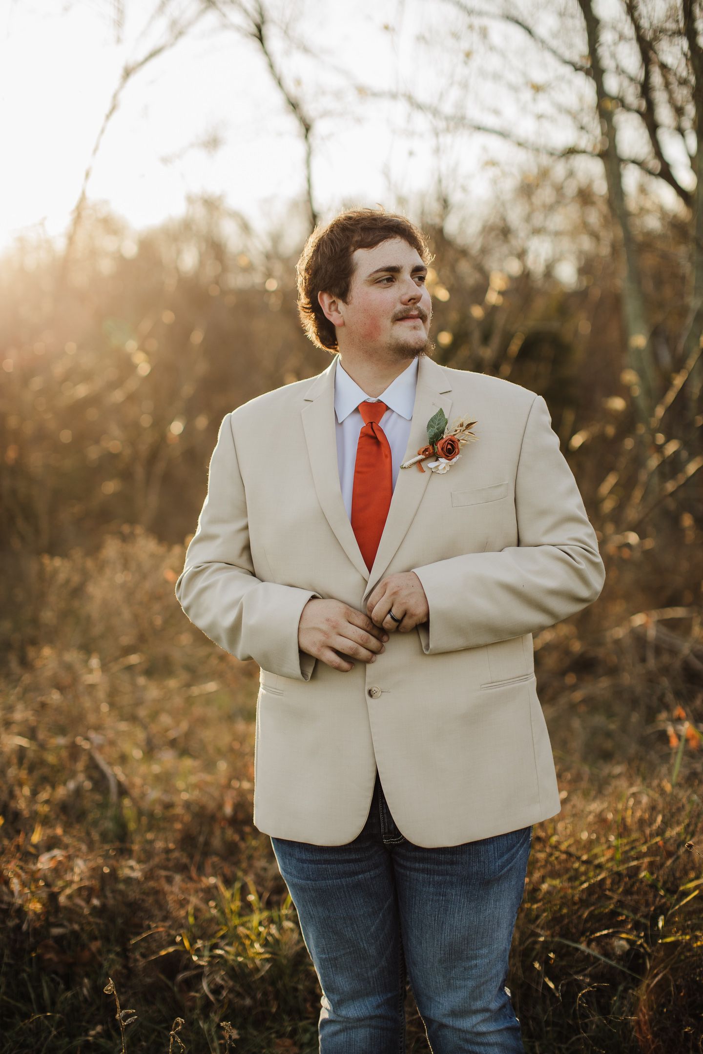 A person in a cream blazer and red tie stands in a golden autumn field during sunset.