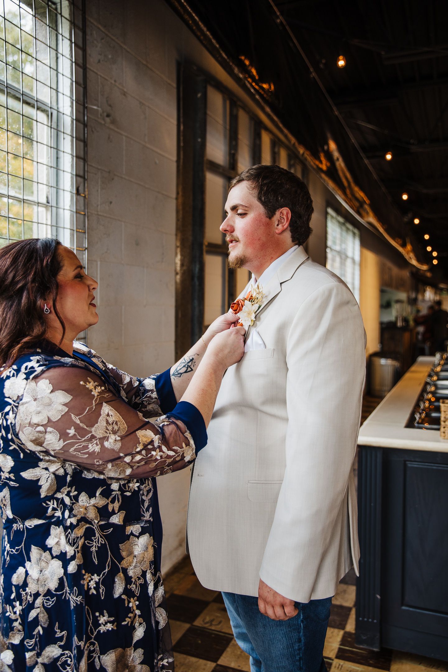 A couple in a restaurant sharing a sweet moment as one adjusts the other's tie, wearing navy floral and white attire.
