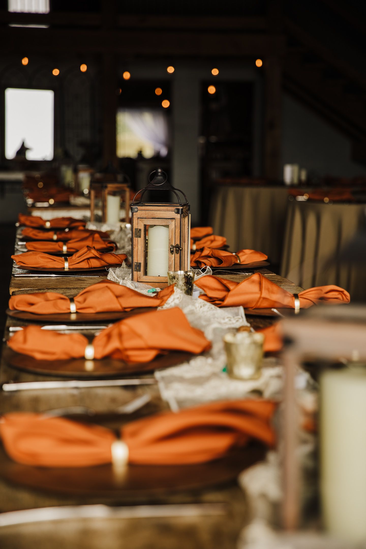 An elegant table setting with orange napkins and lantern centerpieces for a wedding reception.
