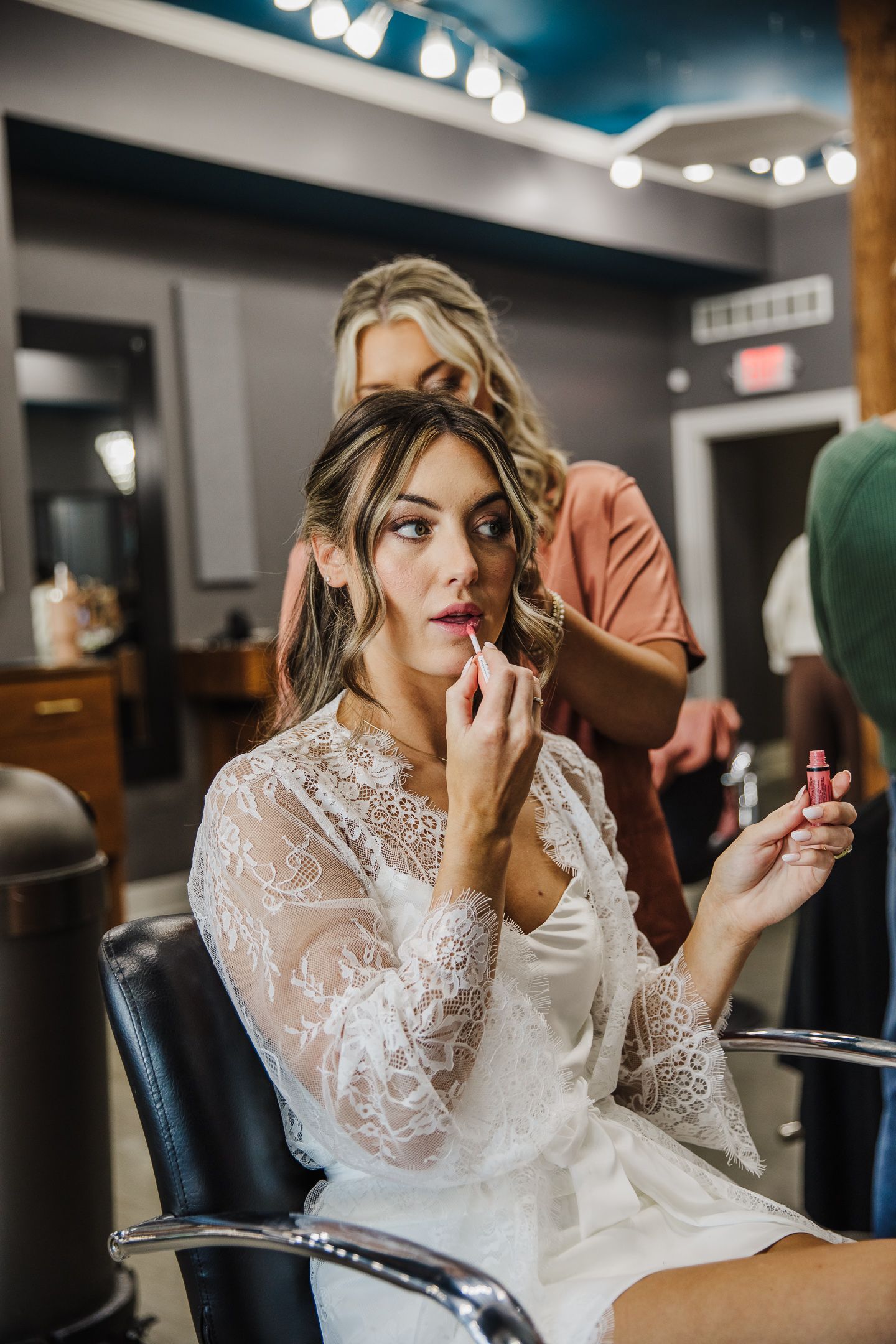 Bride getting final makeup touches in preparation room with blue walls and ambient lighting.