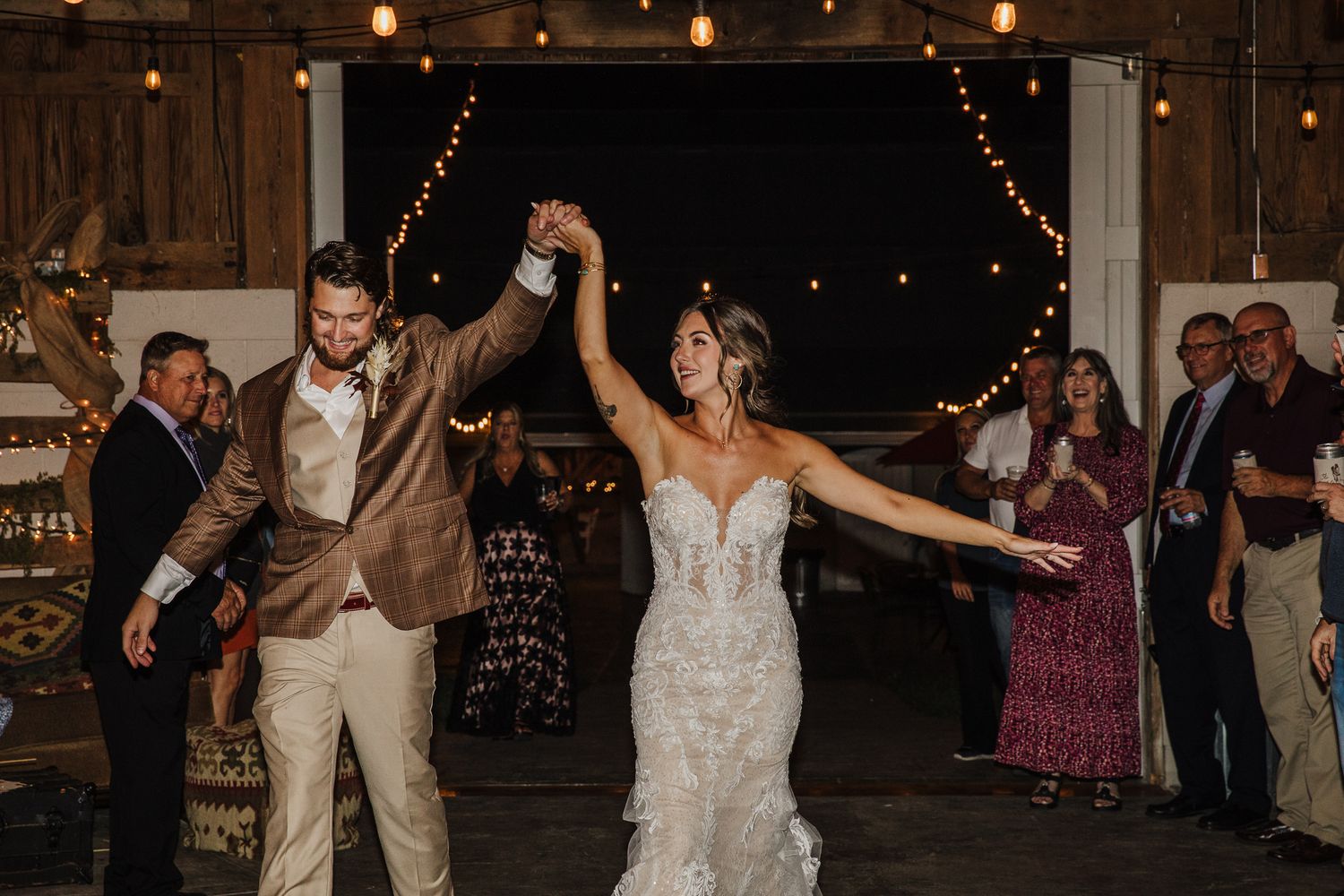 Wedding reception dance party in a dimly lit rustic barn venue with string lights overhead.