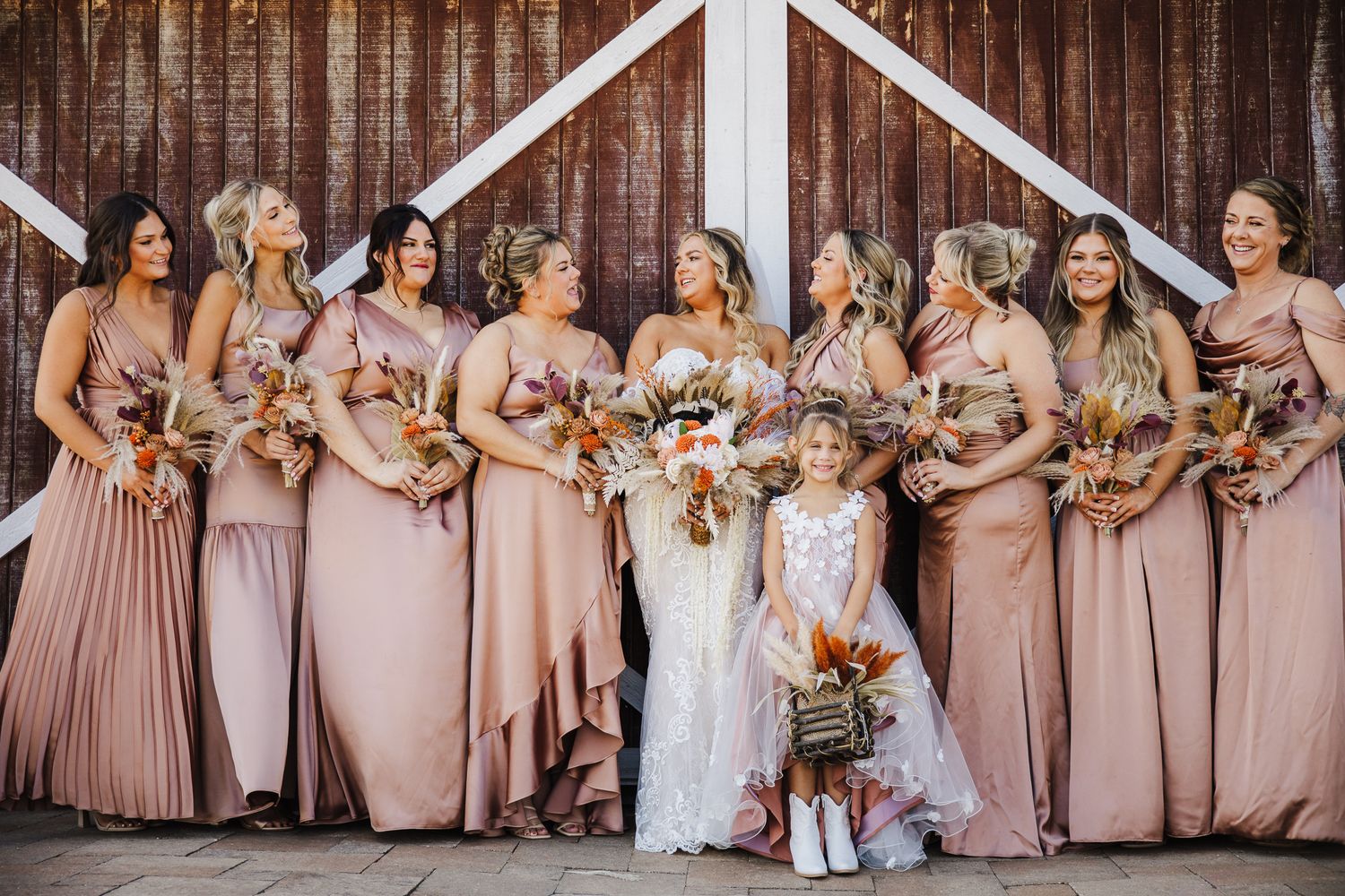 Wedding party wearing blush and mauve colored dresses poses together in a line with autumn bouquets.
