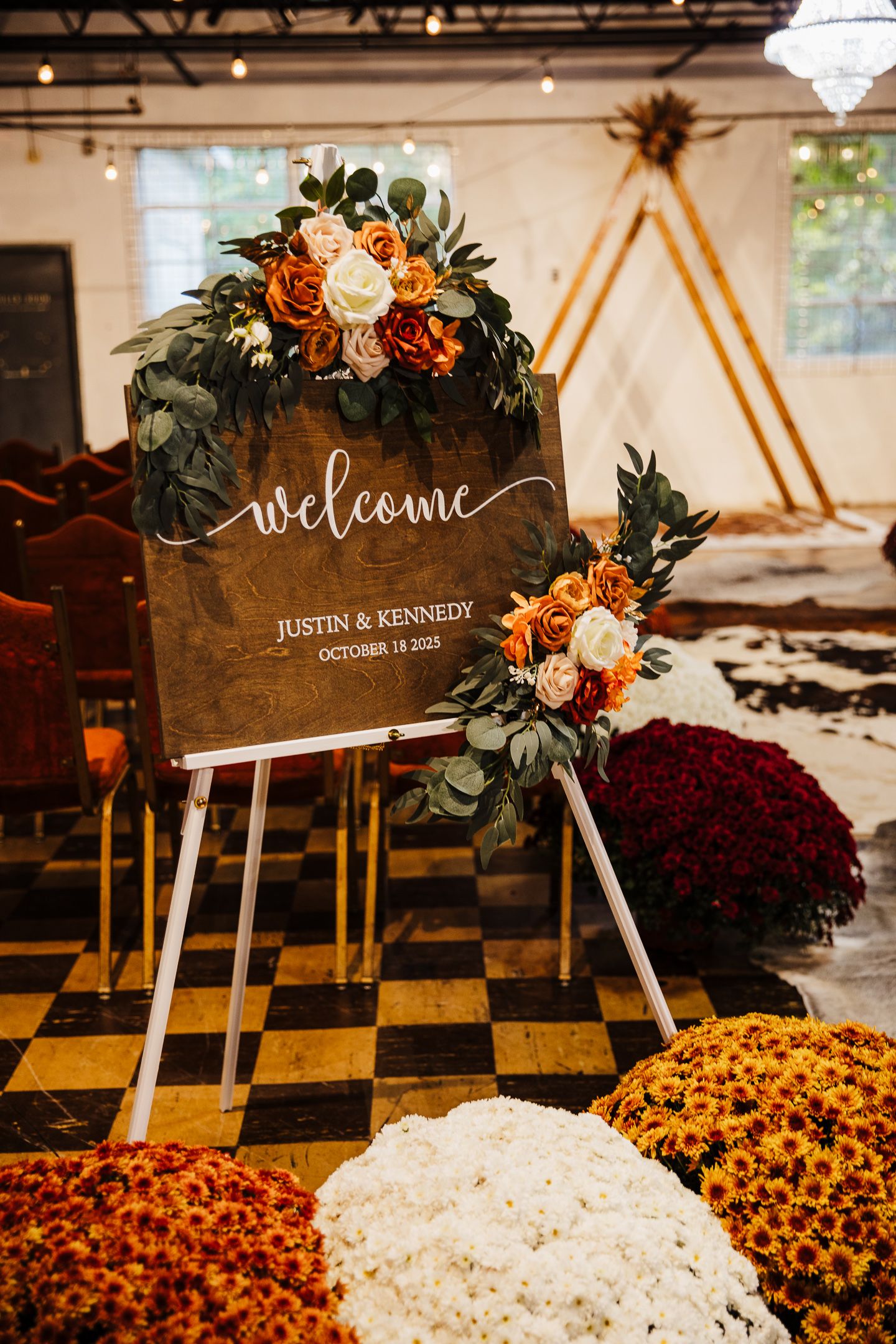 Rustic wooden welcome signs decorated with autumn flowers and greenery at wedding venue entrance.