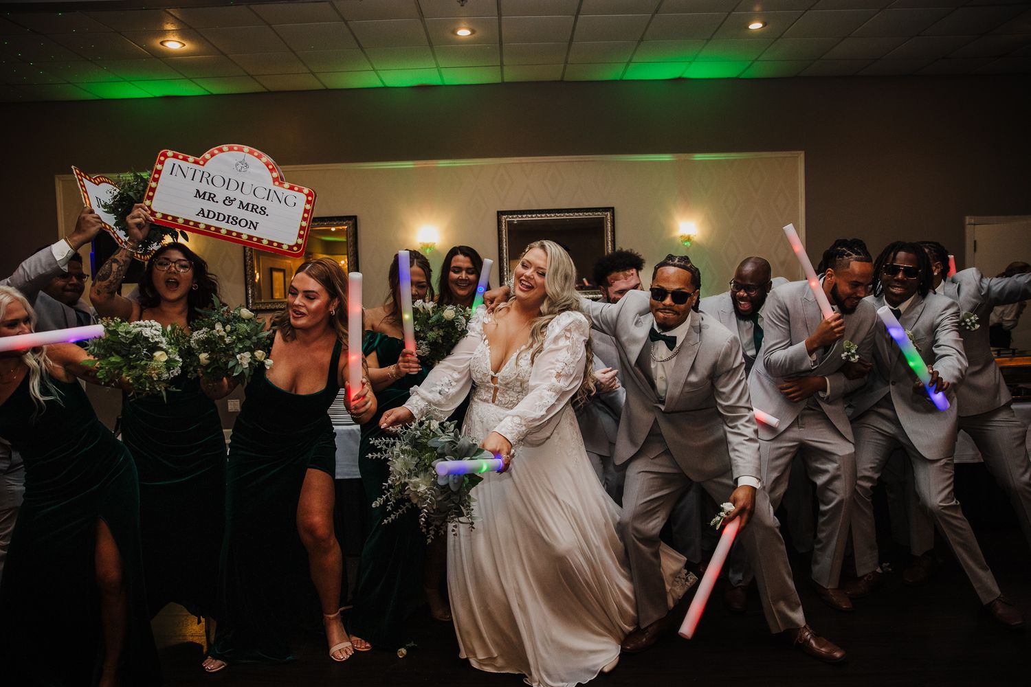 Wedding guests dancing and celebrating on a dimly lit dance floor with green lighting effects in the background.