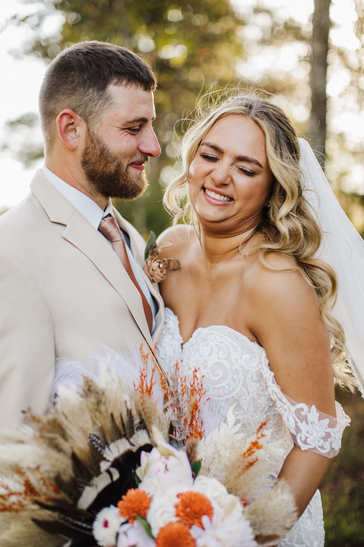 Joyful wedding couple sharing intimate moment among trees in golden afternoon light.