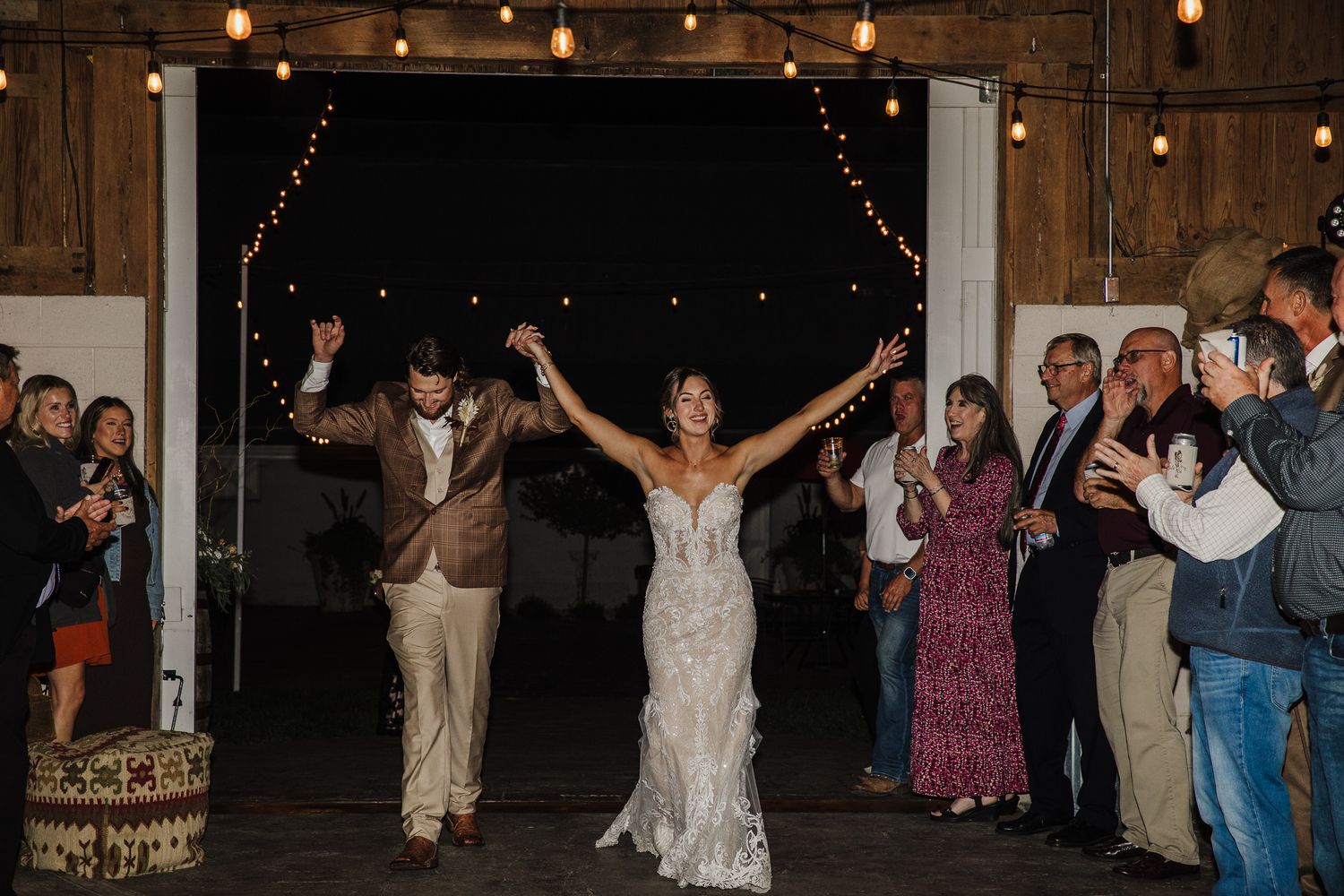 Wedding reception guests dancing and celebrating on a rustic wooden dance floor under string lights.