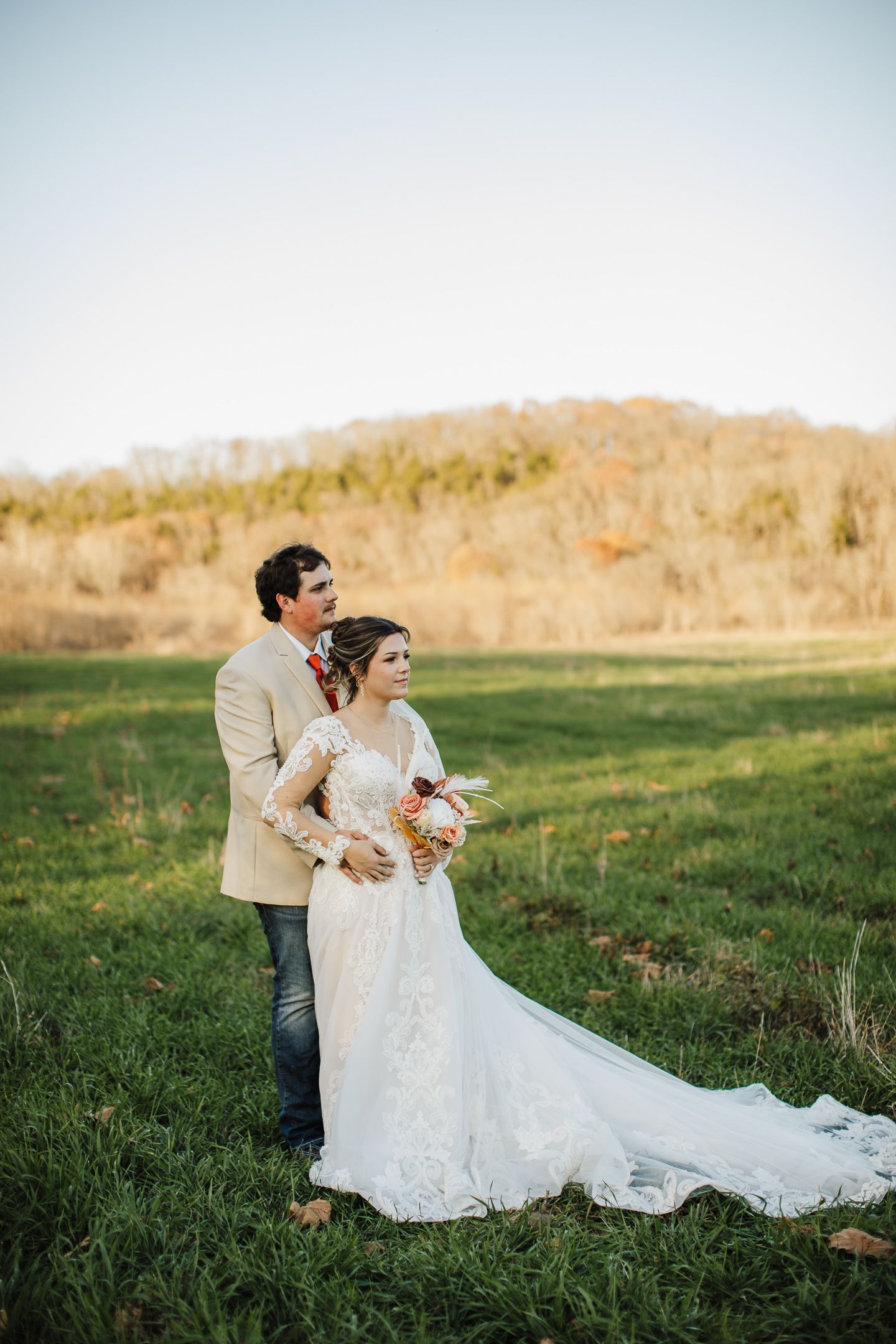 Wedding couple shares tender moments in a scenic field during an autumn sunset photoshoot.