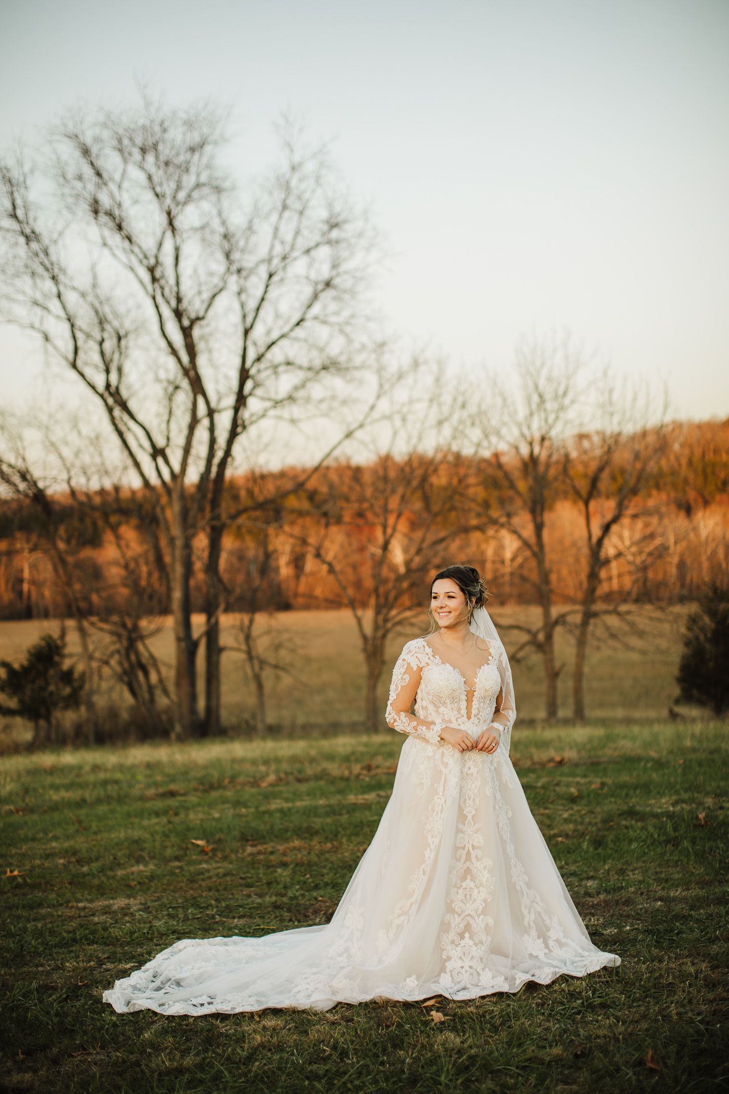 An elegant bridal portrait in a lace gown against an autumn landscape at golden hour.