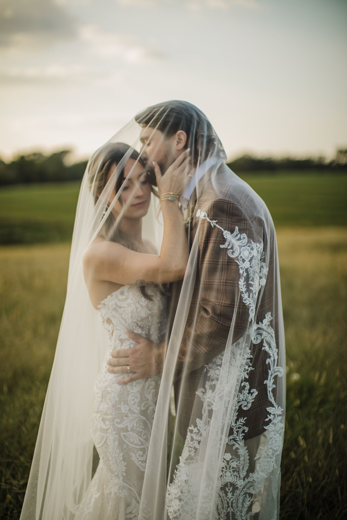 Romantic wedding portrait in a field with a beautifully detailed lace veil catching the sunset light.