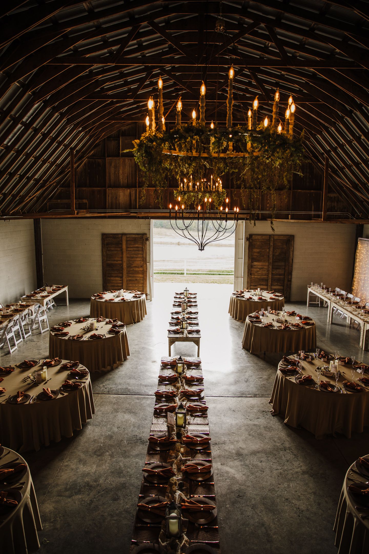 Rustic barn wedding reception venue with elegant chandeliers and long banquet tables set for dining.