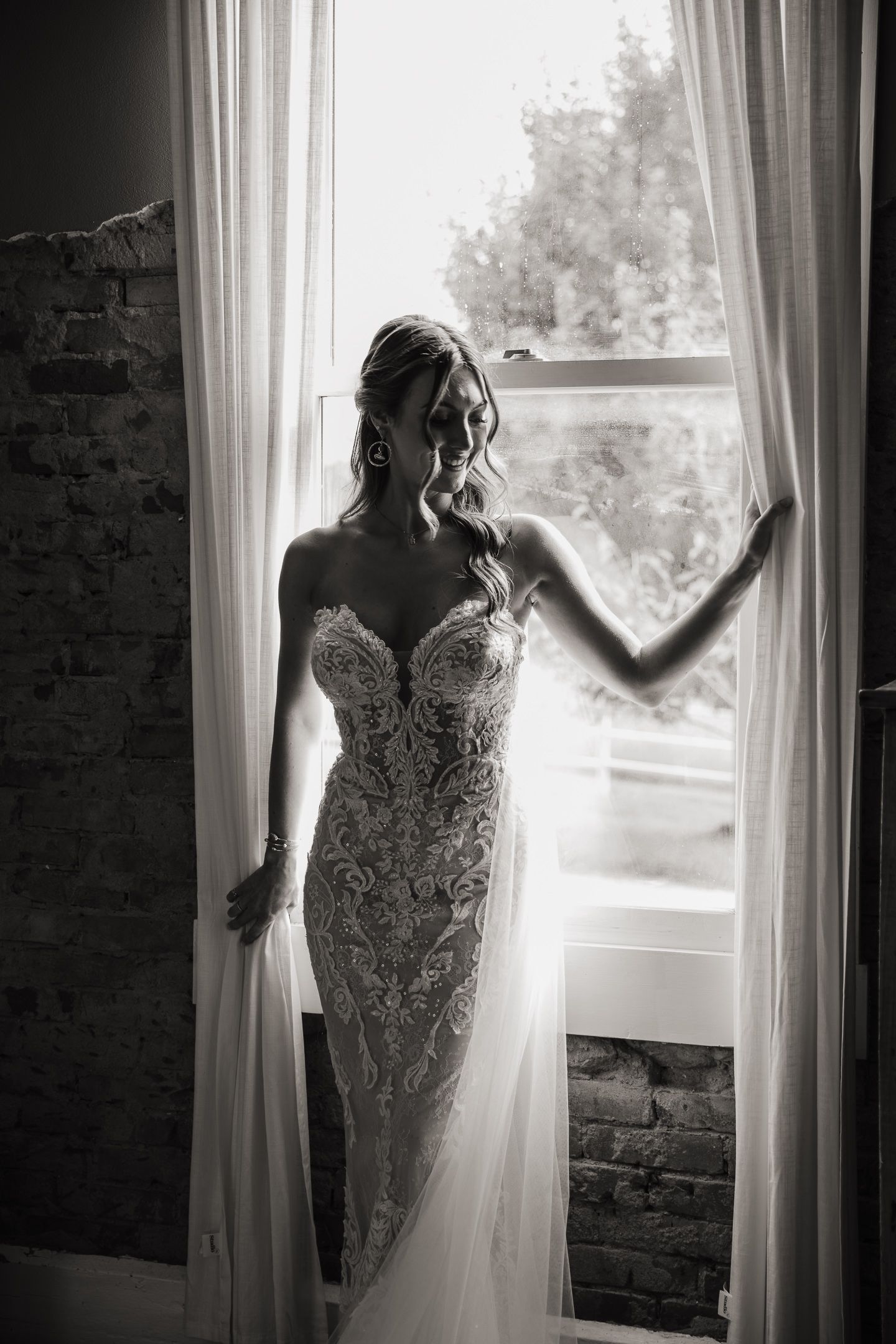 Elegant lace wedding dress silhouette captured through sheer curtains in natural window light.