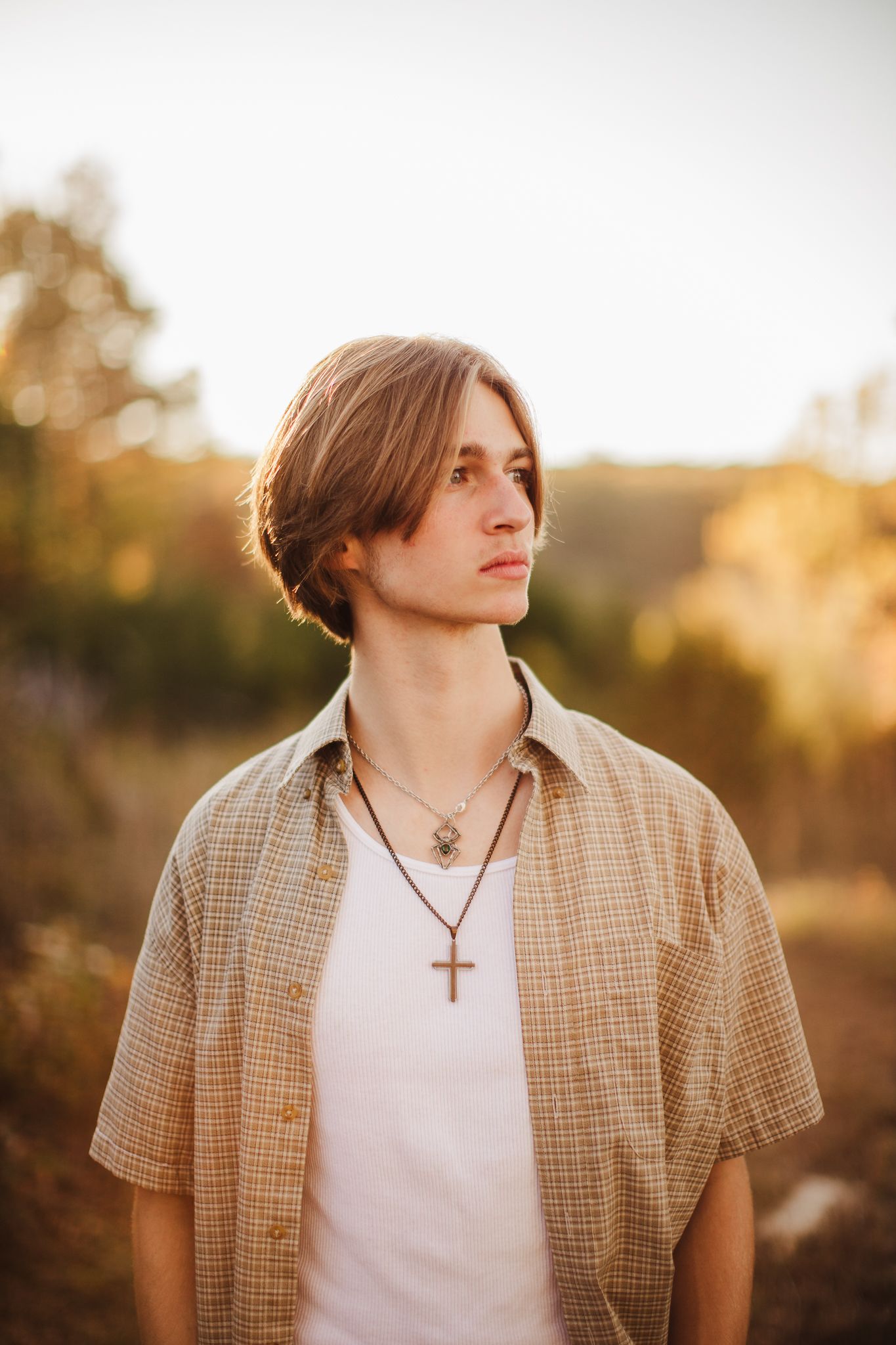 A golden hour portrait featuring a plaid shirt and cross necklace.