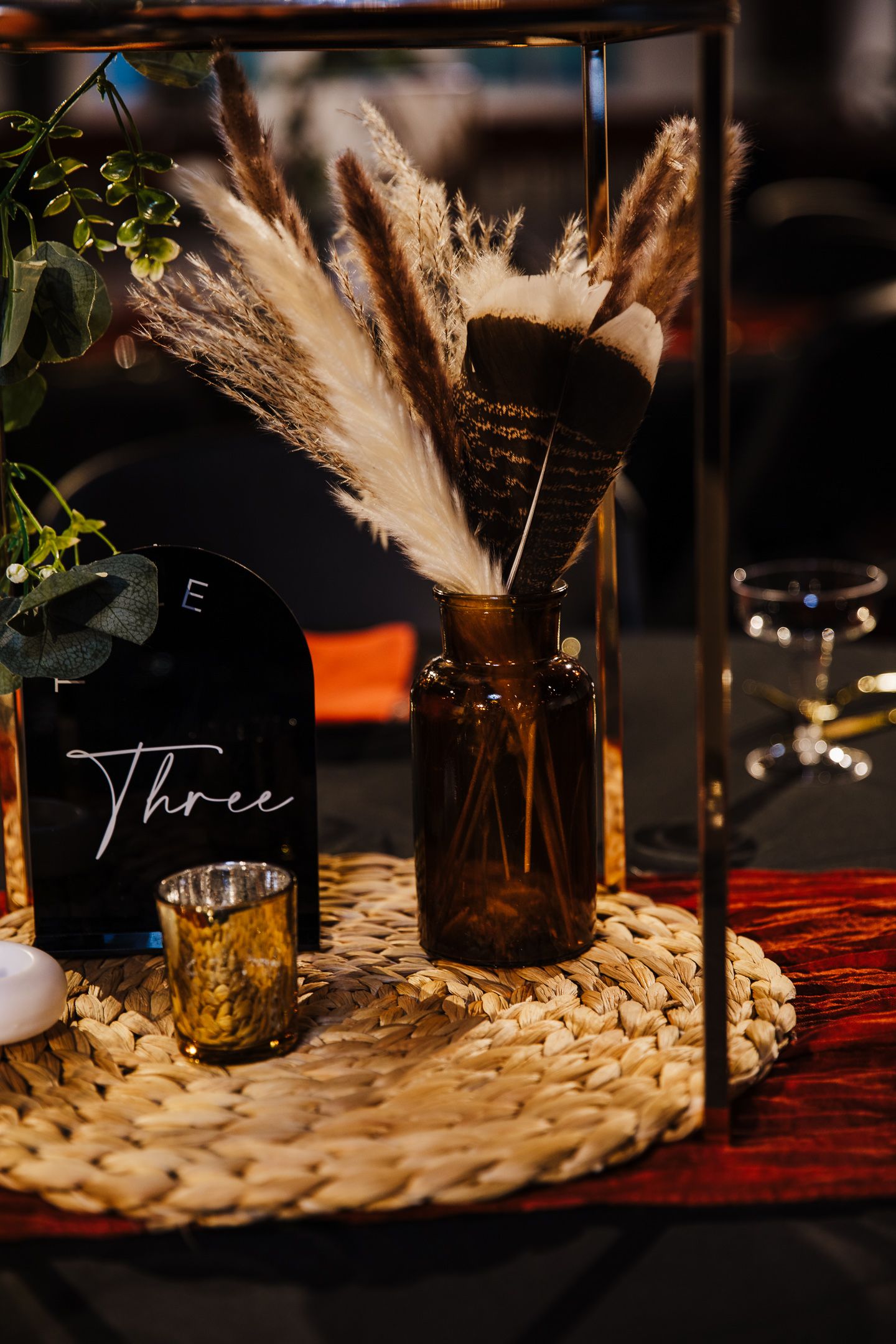 Rustic table setting with amber bottles and dried pampas grass decorations on a woven placemat.
