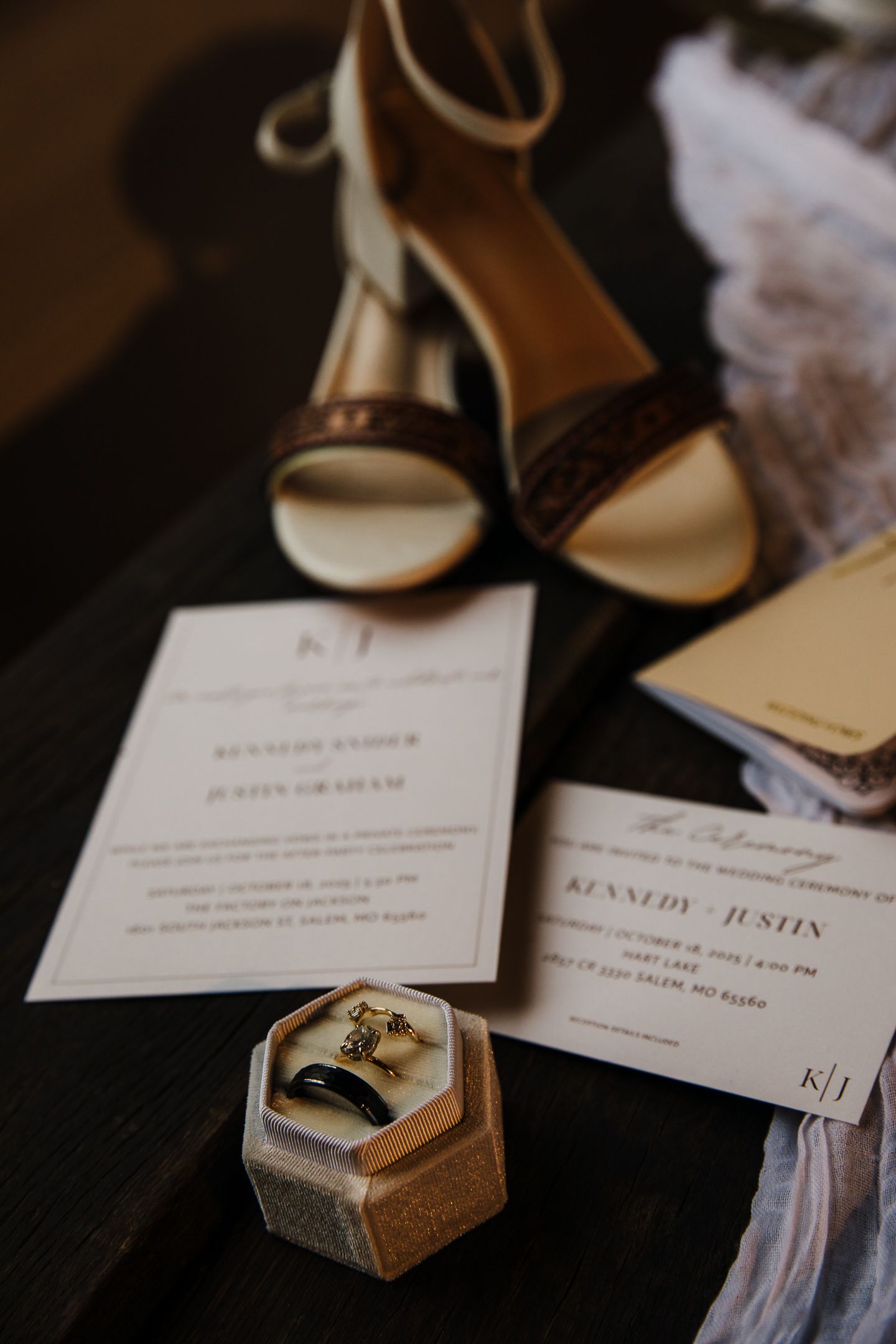 Wedding invitation cards and rings displayed on dark surface with elegant hexagonal ring box.