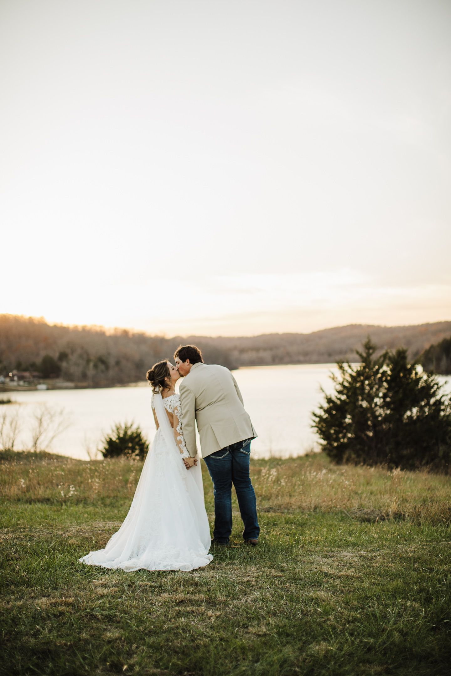 Couple in wedding attire sharing intimate moments during golden hour on a hillside overlooking a tranquil lake.