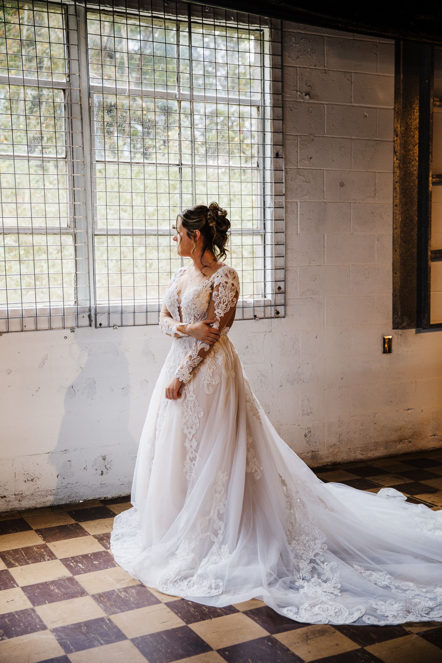 Elegant lace wedding gown with flowing train in industrial venue with checkered floor.