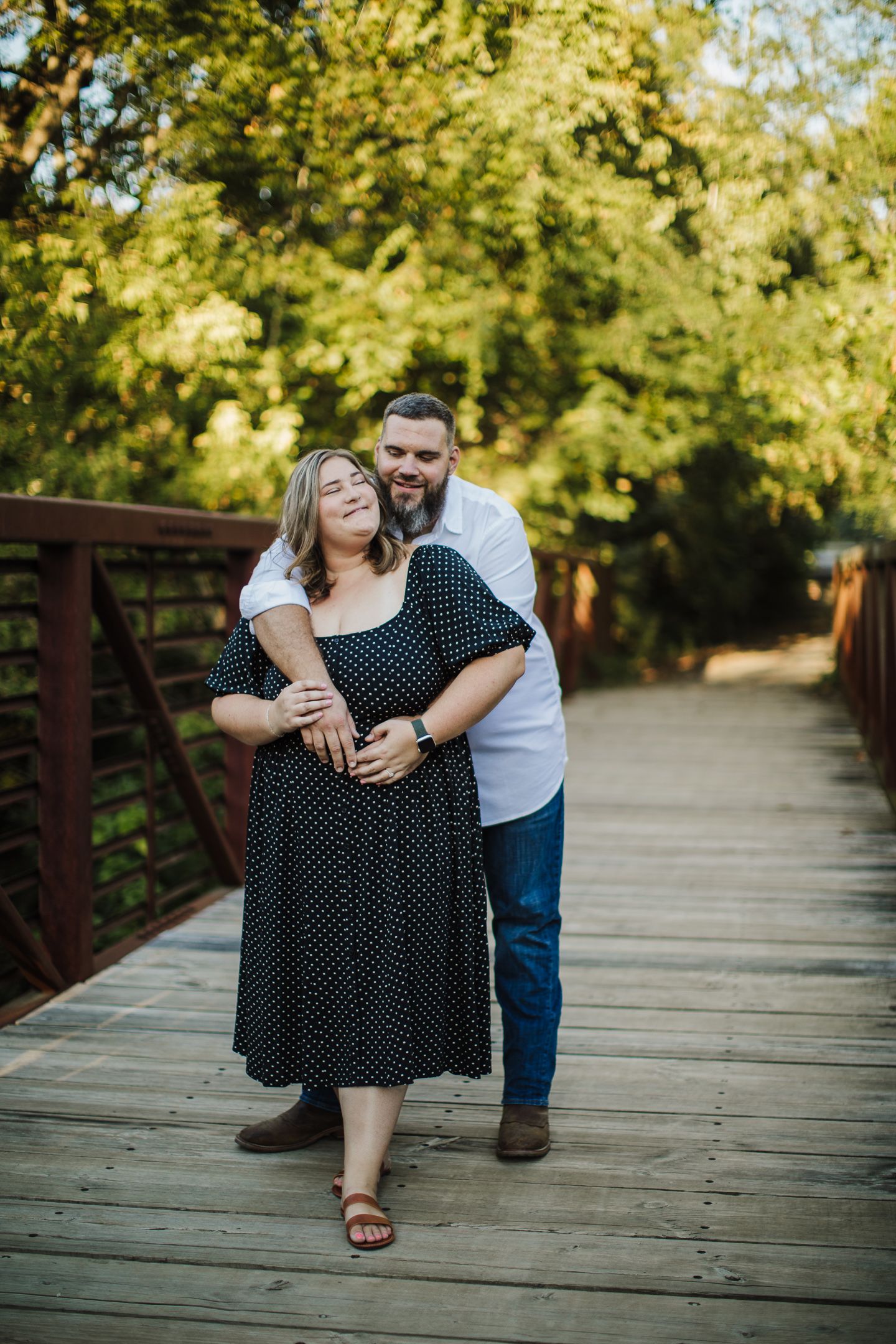 Couple sharing playful moments on wooden bridge surrounded by lush greenery.