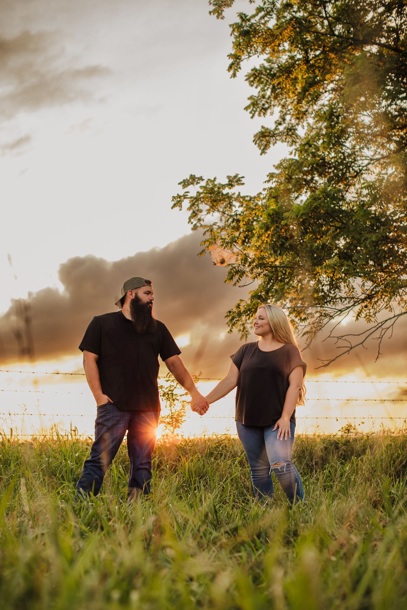 Silhouetted couple walking through a grassy field at sunset with golden light and trees.