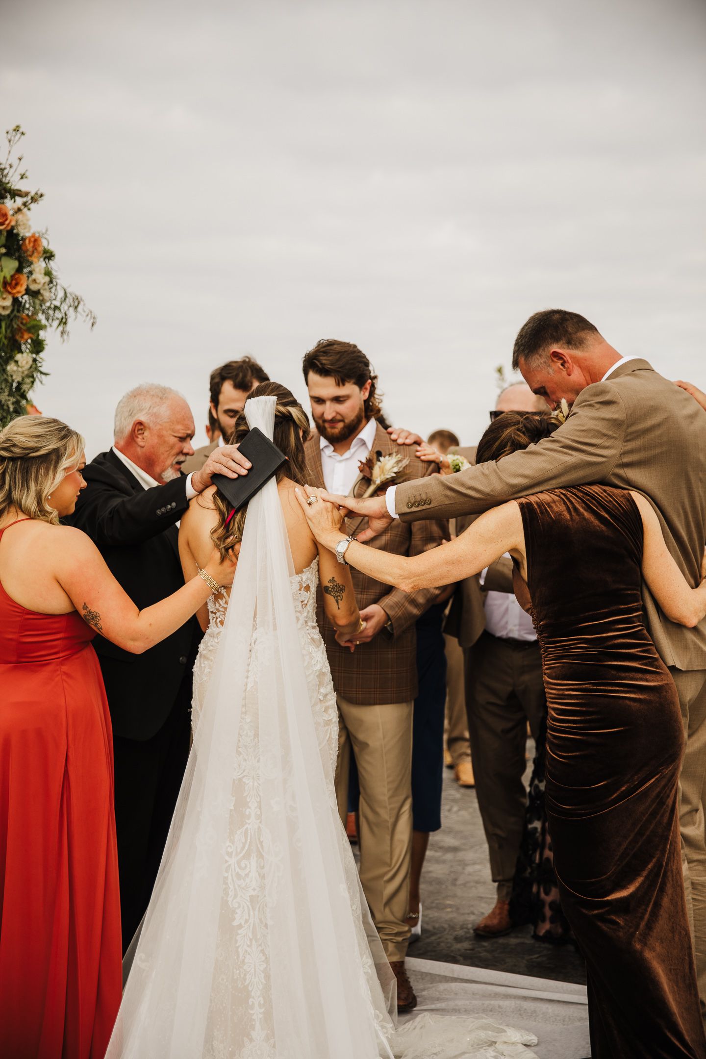 Wedding party gathers around couple for emotional group prayer moment.