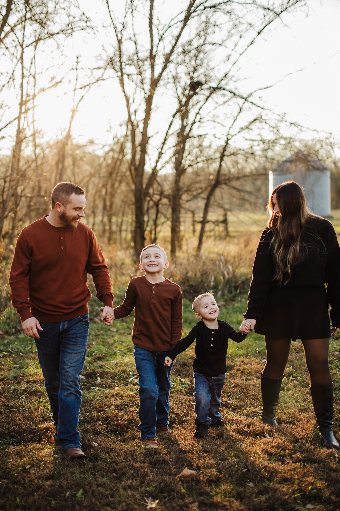 A family holds hands while walking together on a wooded trail during golden hour.