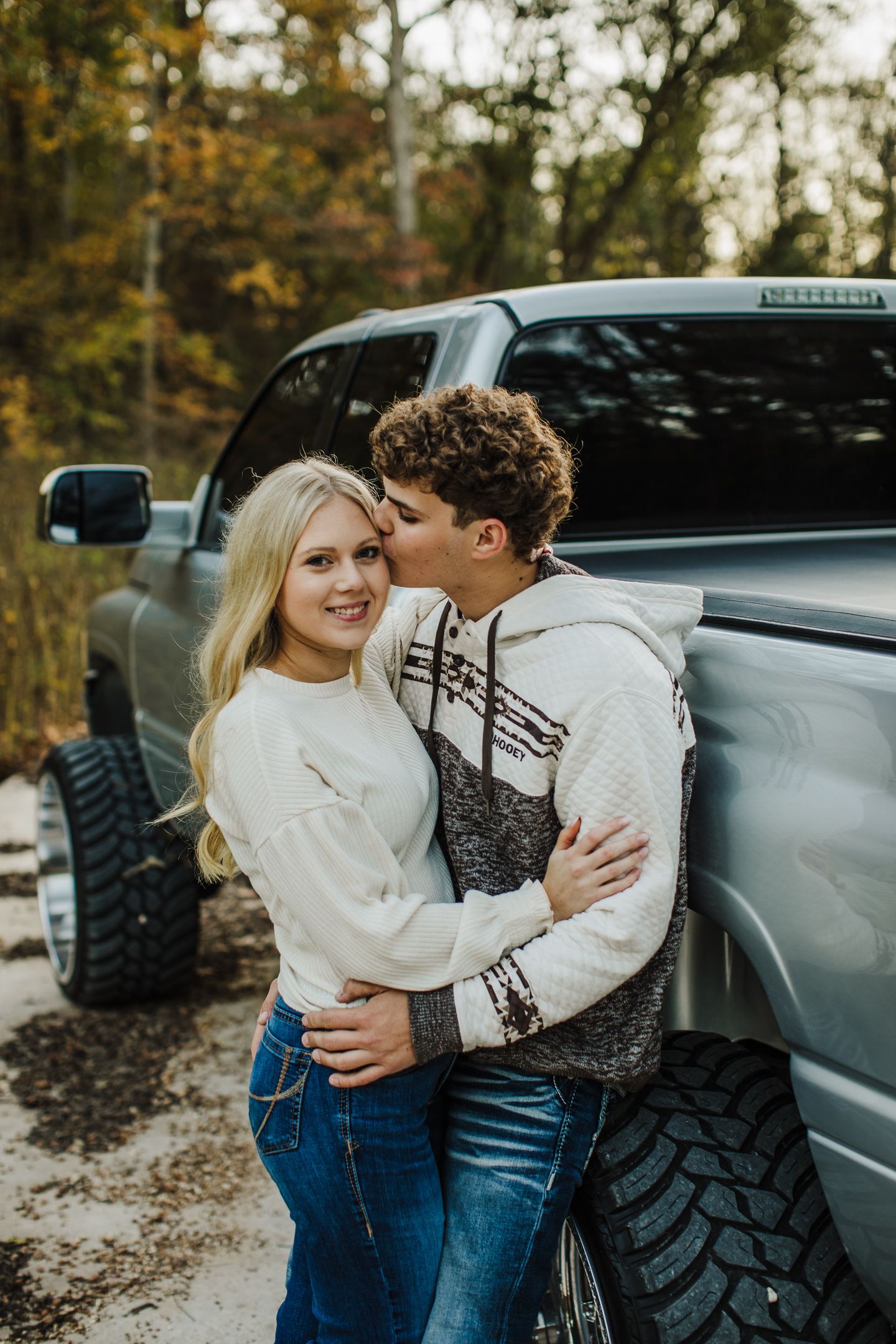 A couple poses affectionately against a truck during an autumn photoshoot.